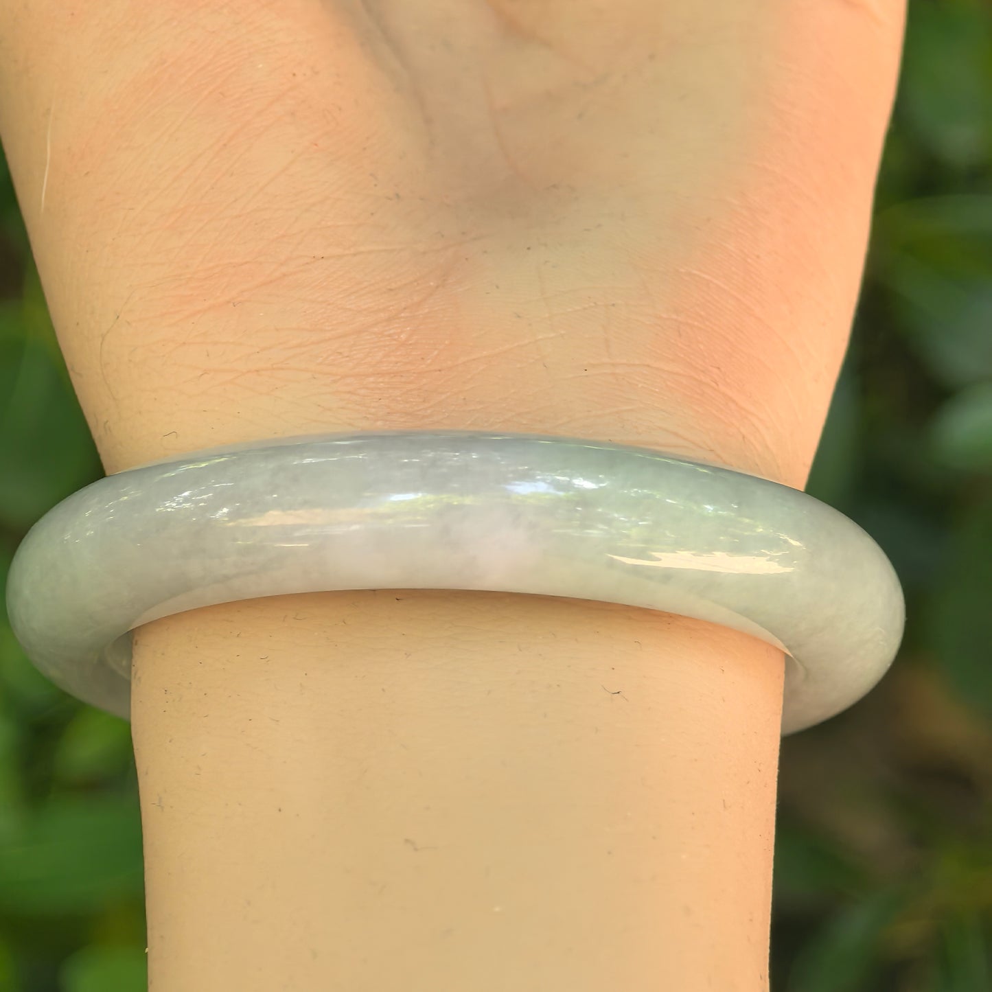 Glutinous pale green D-shape jadeite bangle displayed on wrist with gentle natural luster.

