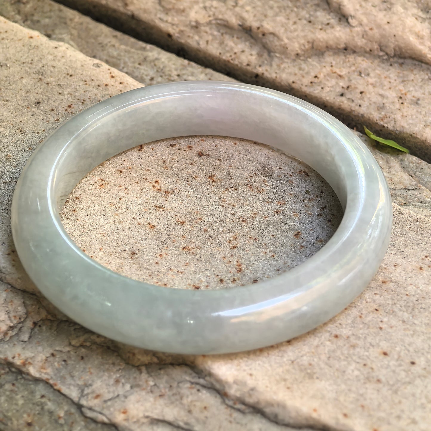 Angled view of glutinous pale green jadeite bangle resting on stone background.
