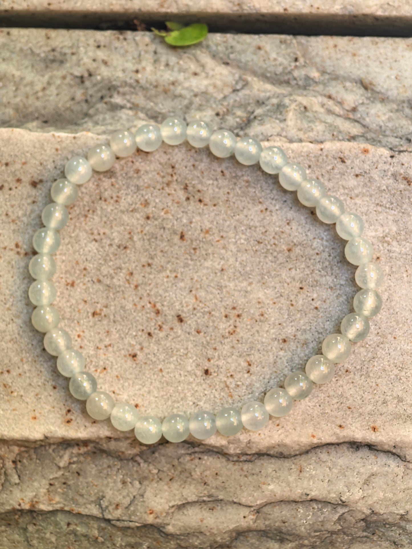 Natural Grade-A icy white-green jadeite bead bracelet arranged on stone, showing 37 small round beads.
