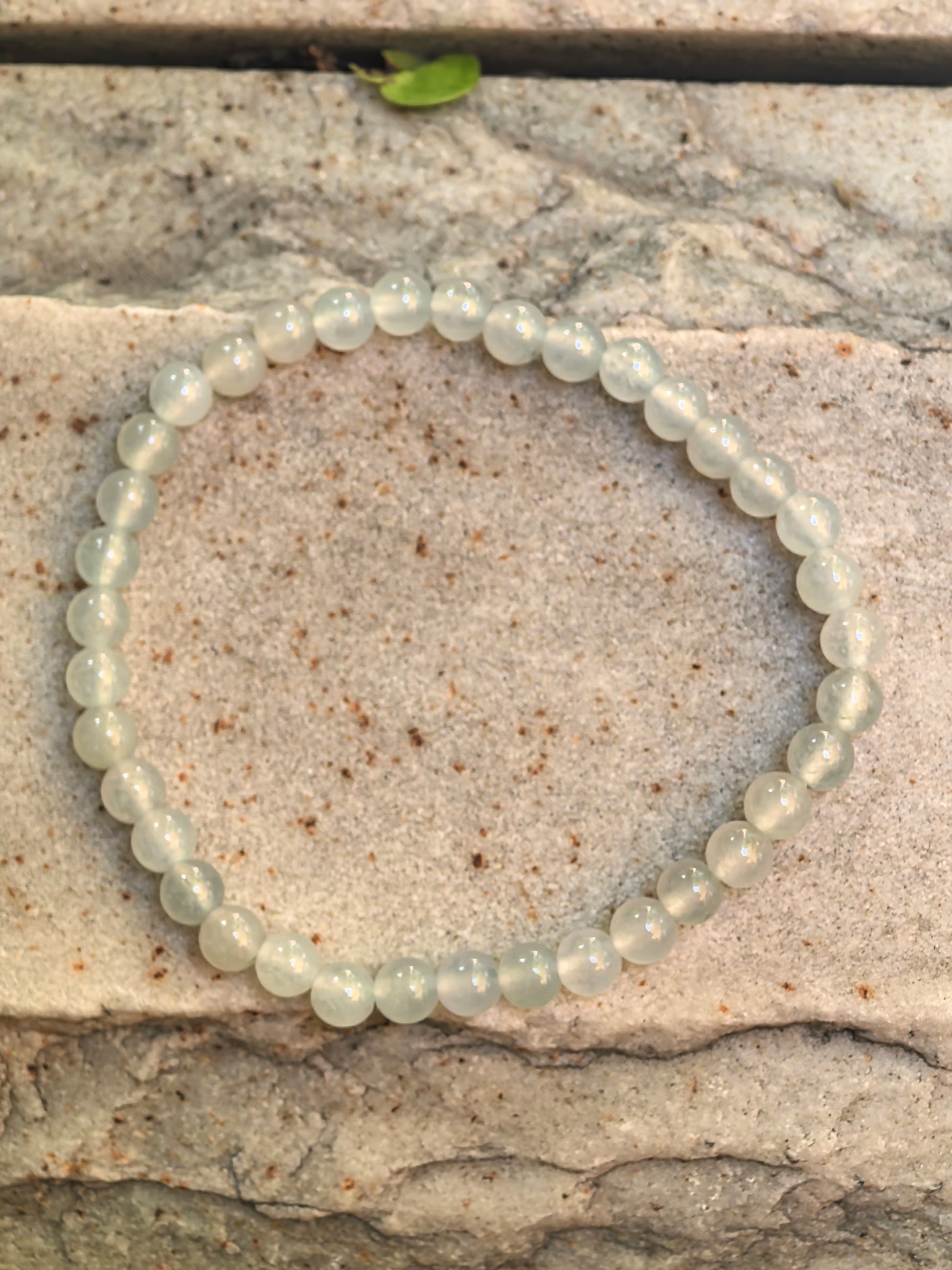 Natural Grade-A icy white-green jadeite bead bracelet arranged on stone, showing 37 small round beads.

