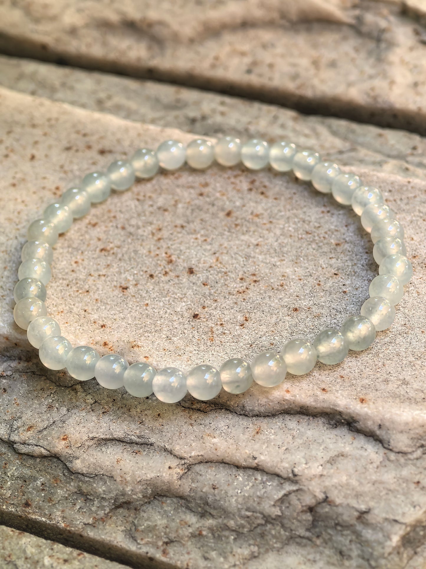 Close-up of icy white-green jadeite bead bracelet on stone with soft translucency and polished round beads.
