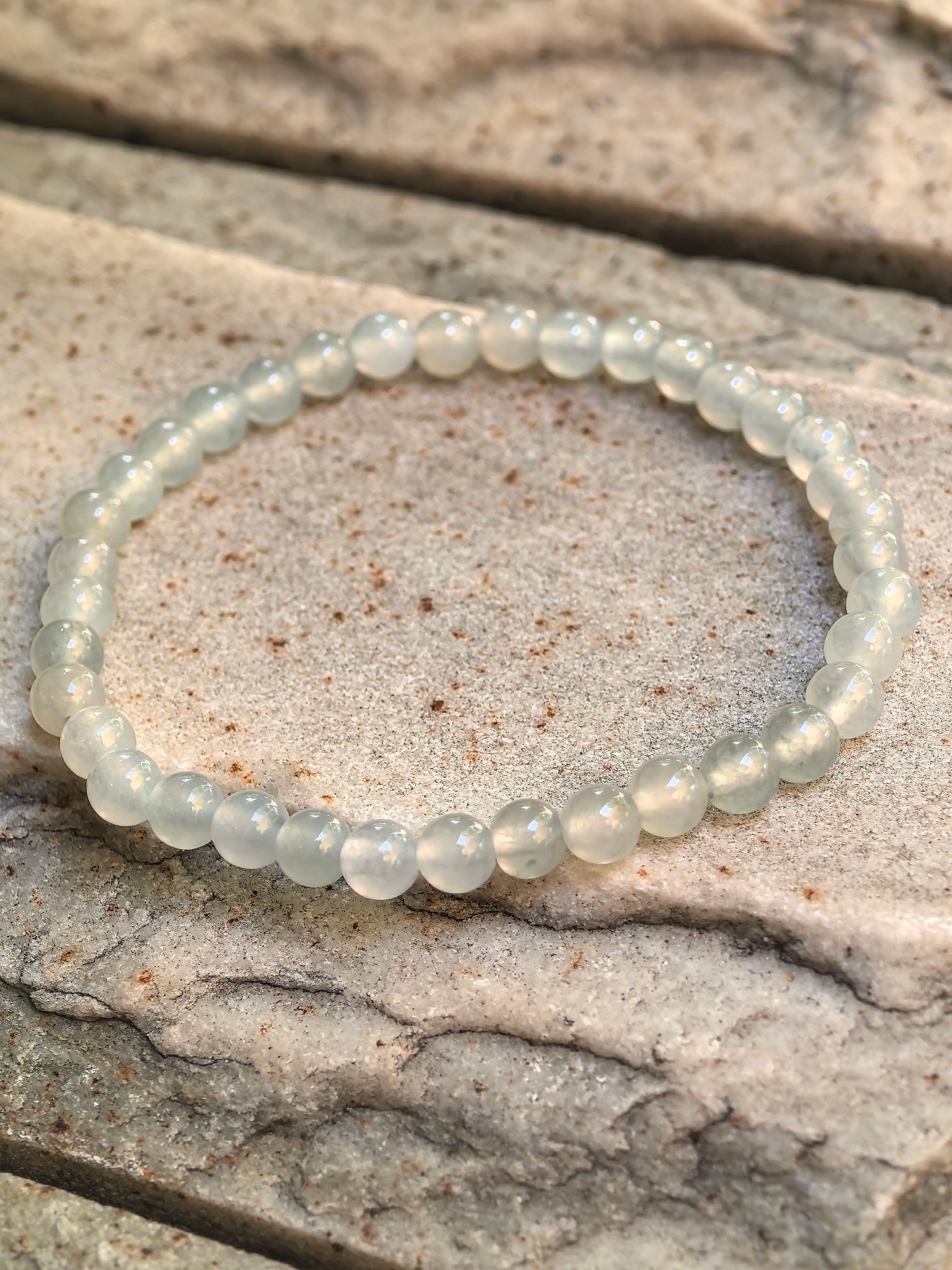 Close-up of icy white-green jadeite bead bracelet on stone with soft translucency and polished round beads.
