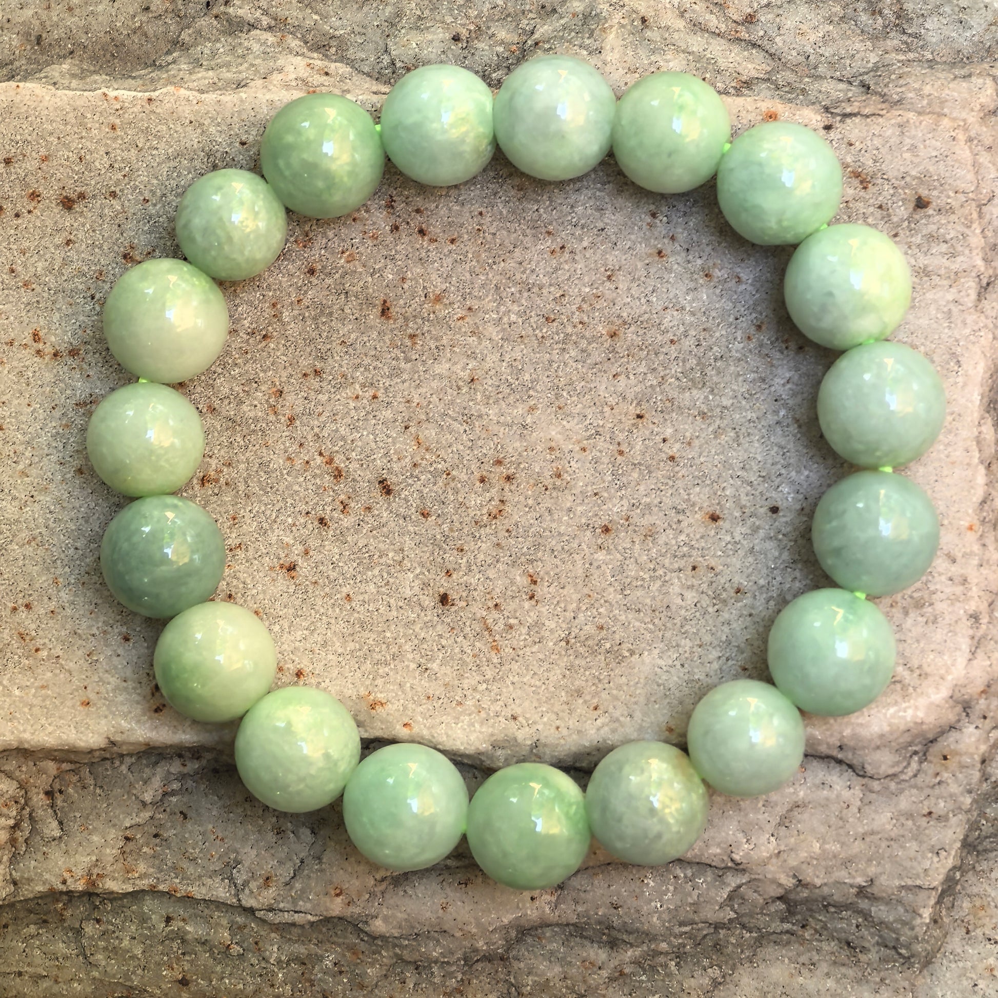 Natural Grade-A apple green jadeite bead bracelet arranged on stone, showing 19 round beads and soft color variation.
