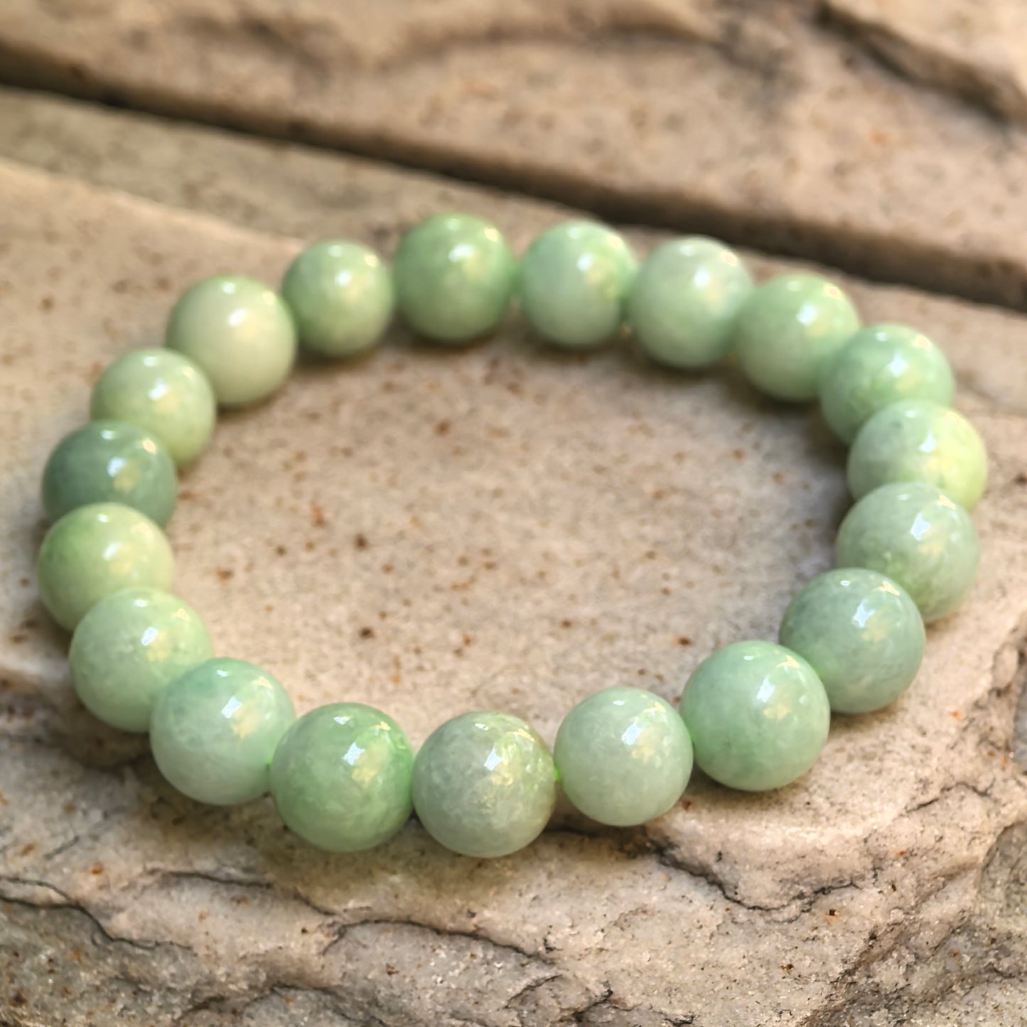 Angled view of apple green jadeite round bead bracelet on stone surface with natural internal texture.
