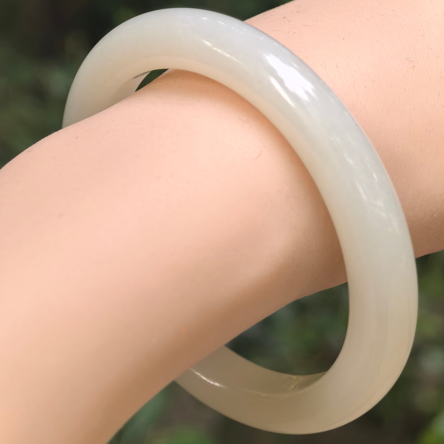 Natural Hetian jade bangle worn on wrist, showing a smooth rounded profile and soft white-green tone.