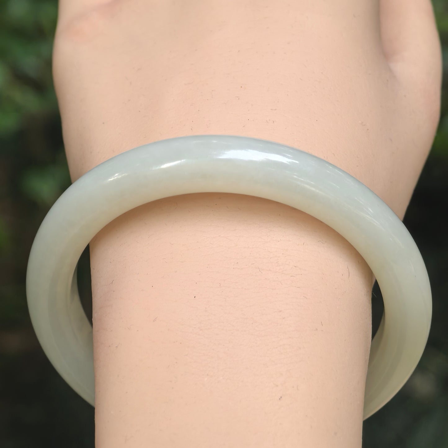 Close-up of white-green Hetian jade bangle on wrist with glossy polish and gentle natural translucency.