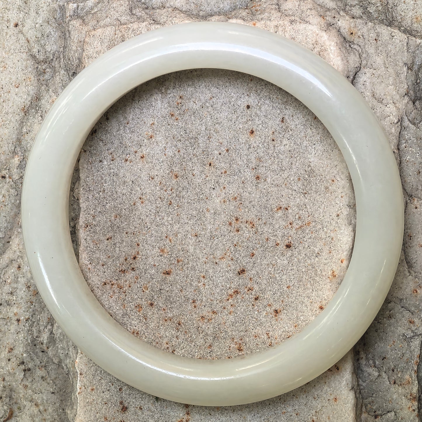 Top view of round Hetian jade bangle on stone background, showing its clean circular shape and pale green-white color.