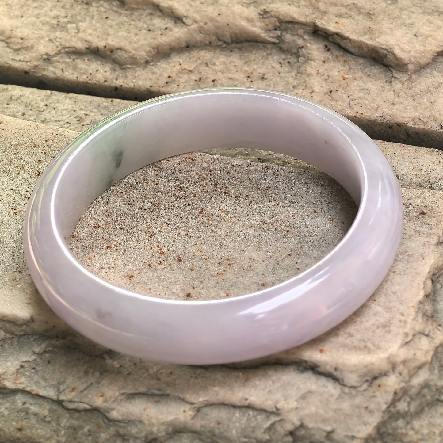 Side view of glutinous lavender jadeite bangle showing fuller width and polished curved surface.