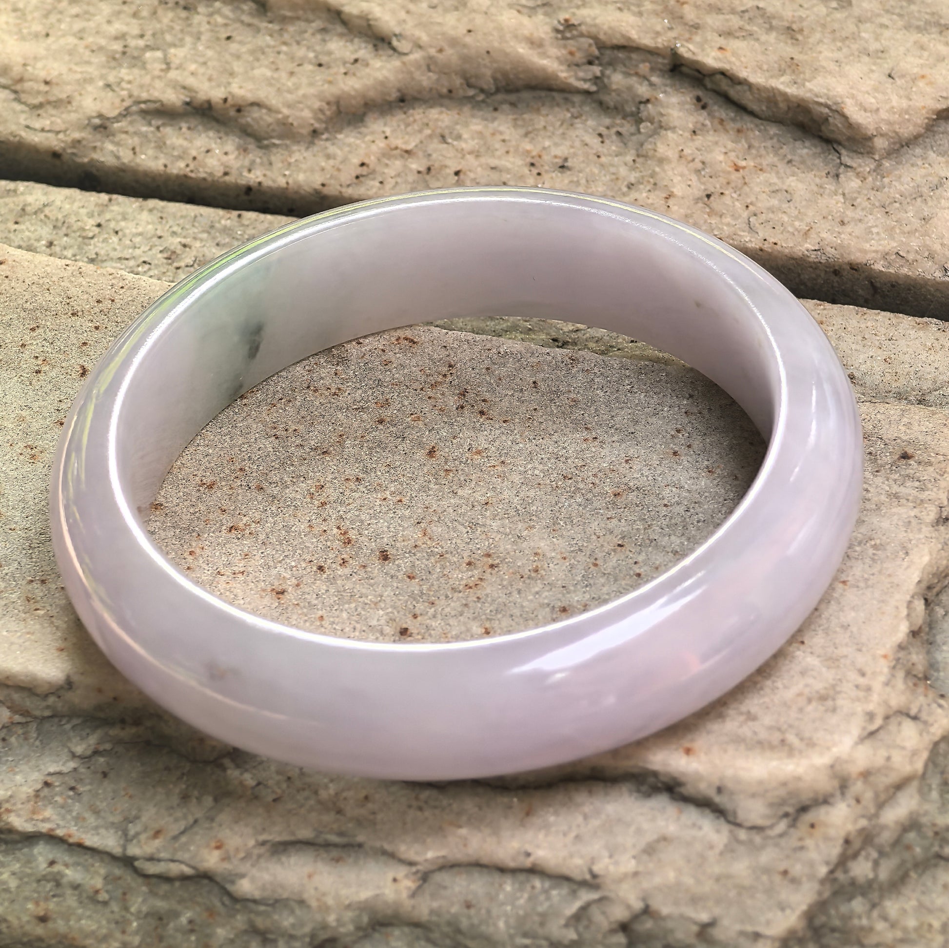Side view of glutinous lavender jadeite bangle showing fuller width and polished curved surface.
