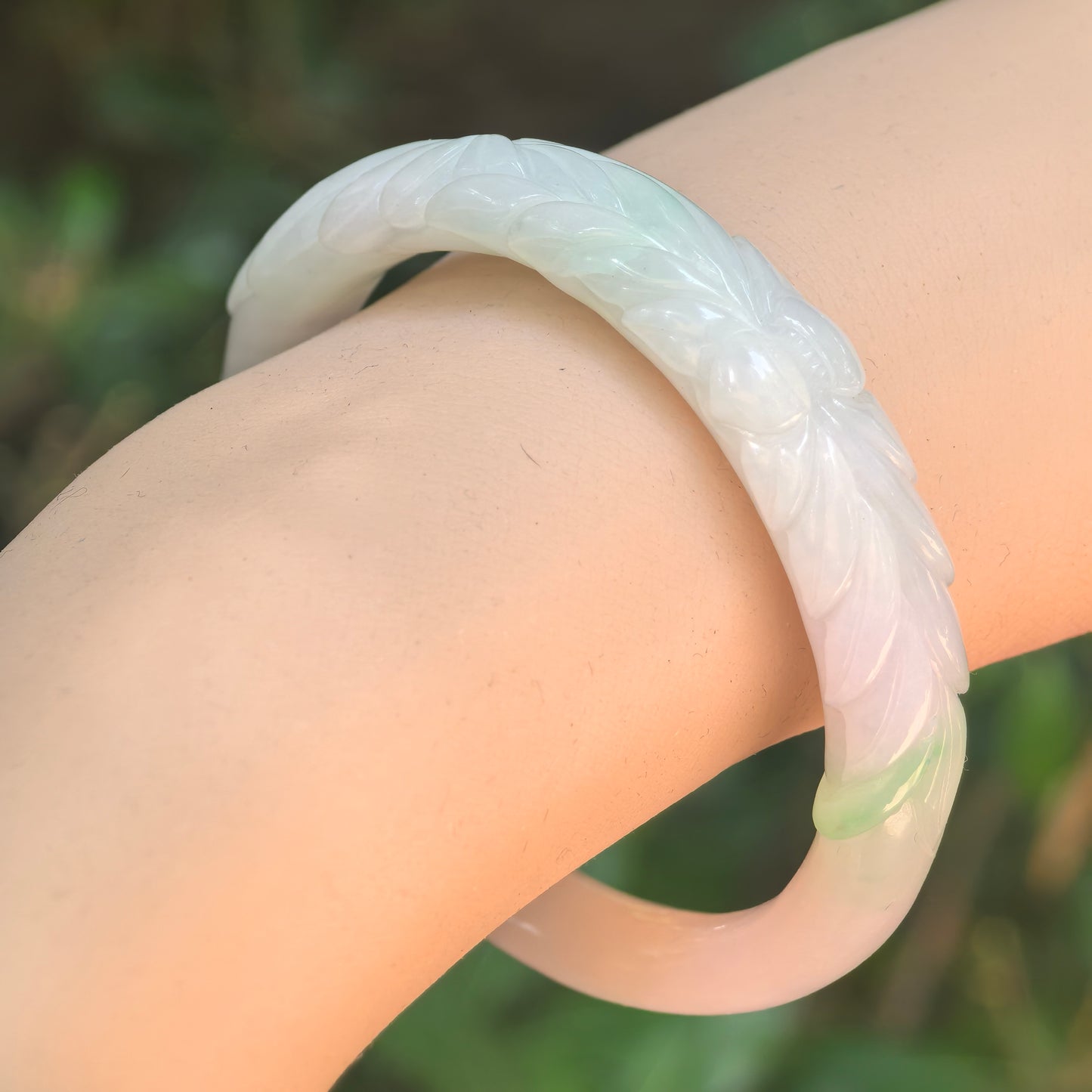 Natural Grade-A glutinous white-and-green floral oval jadeite bangle worn on wrist under natural light.
