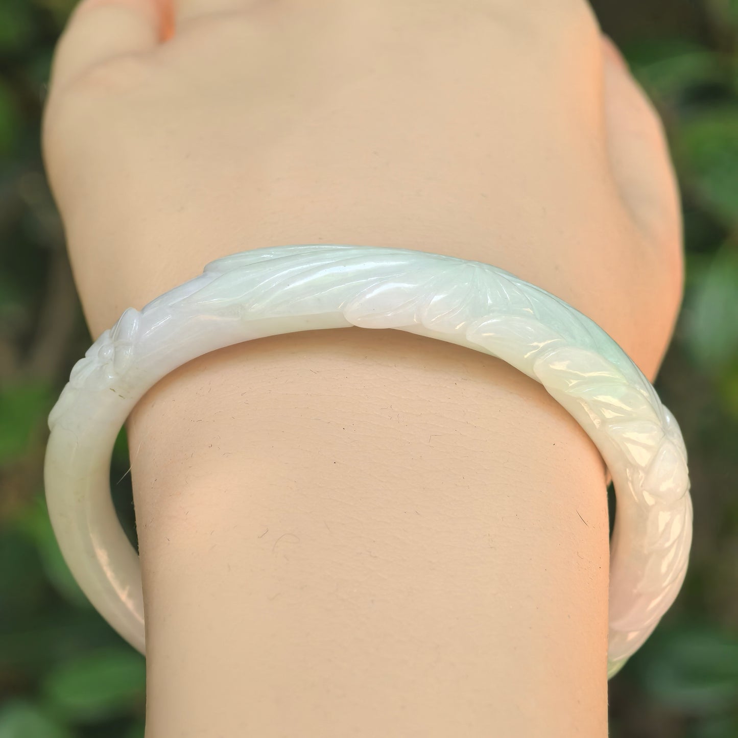 Close-up of carved floral jadeite bangle showing white base and soft green accent.
