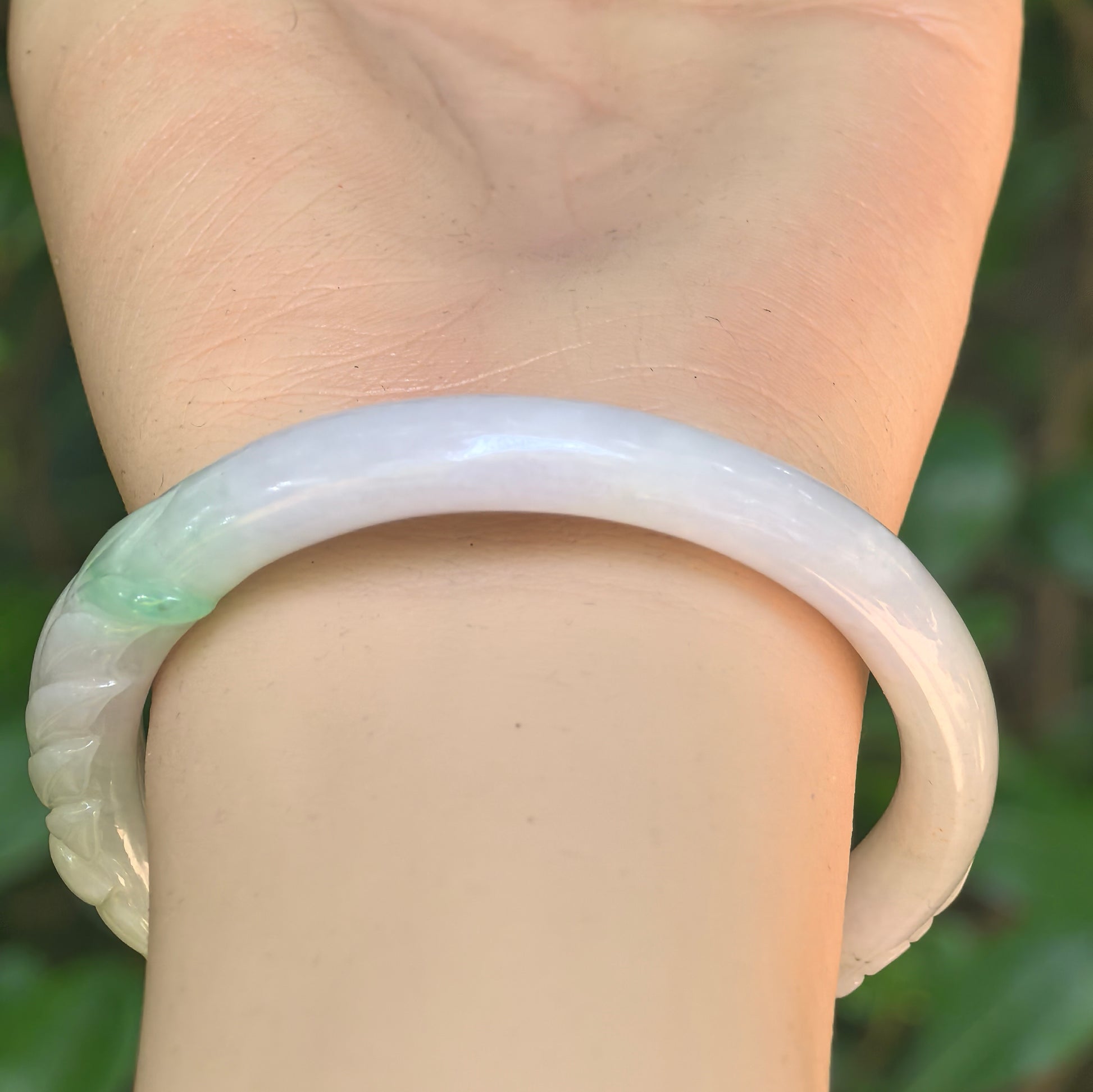 Glutinous white-and-green oval jadeite bangle on wrist showing carved leaf motif and smooth luster.
