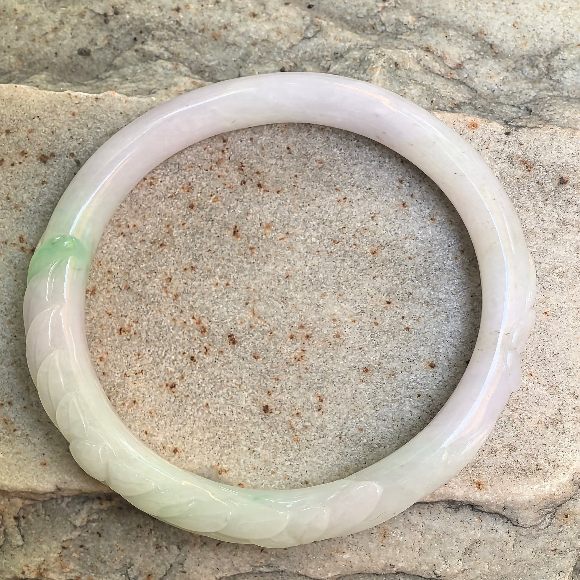 Top view of white-and-green carved oval jadeite bangle showing Guifei shape and floral detail.
