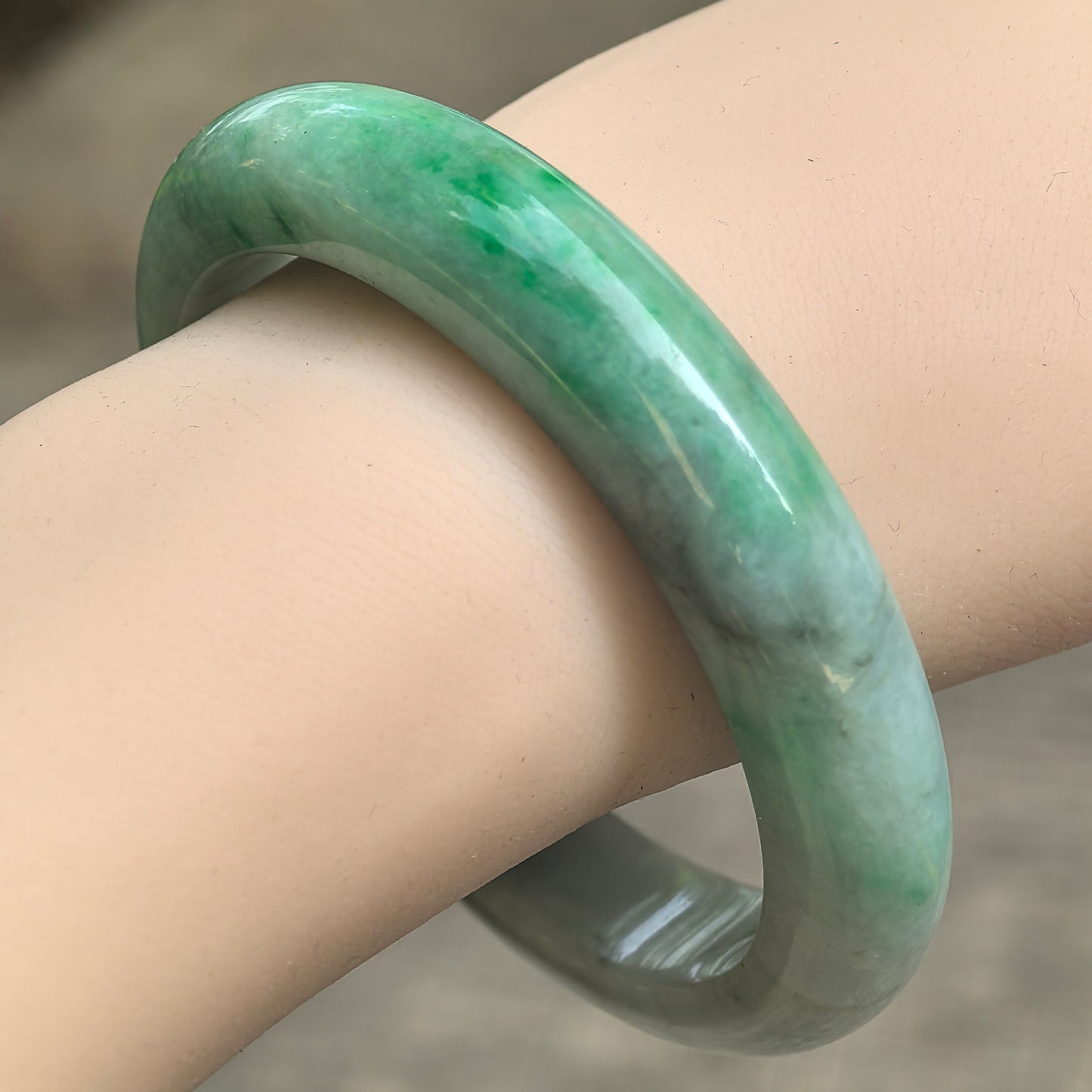 Natural Grade-A white-base green jadeite D-shape bangle shown on wrist under natural light, 58mm inner diameter.
