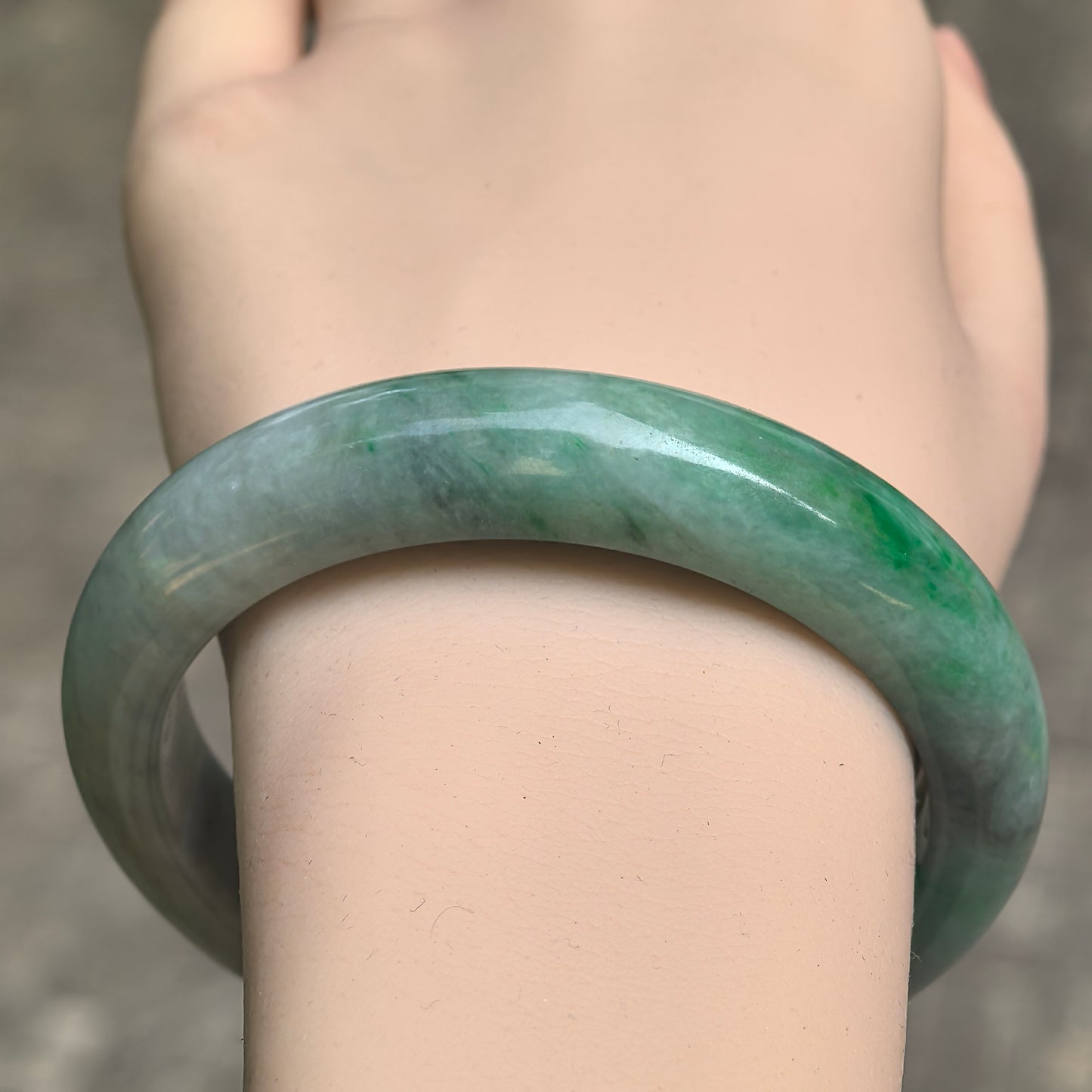 Close-up wrist view of glutinous jadeite bangle with pale green tone, smooth polish, and rounded D-shape profile.
