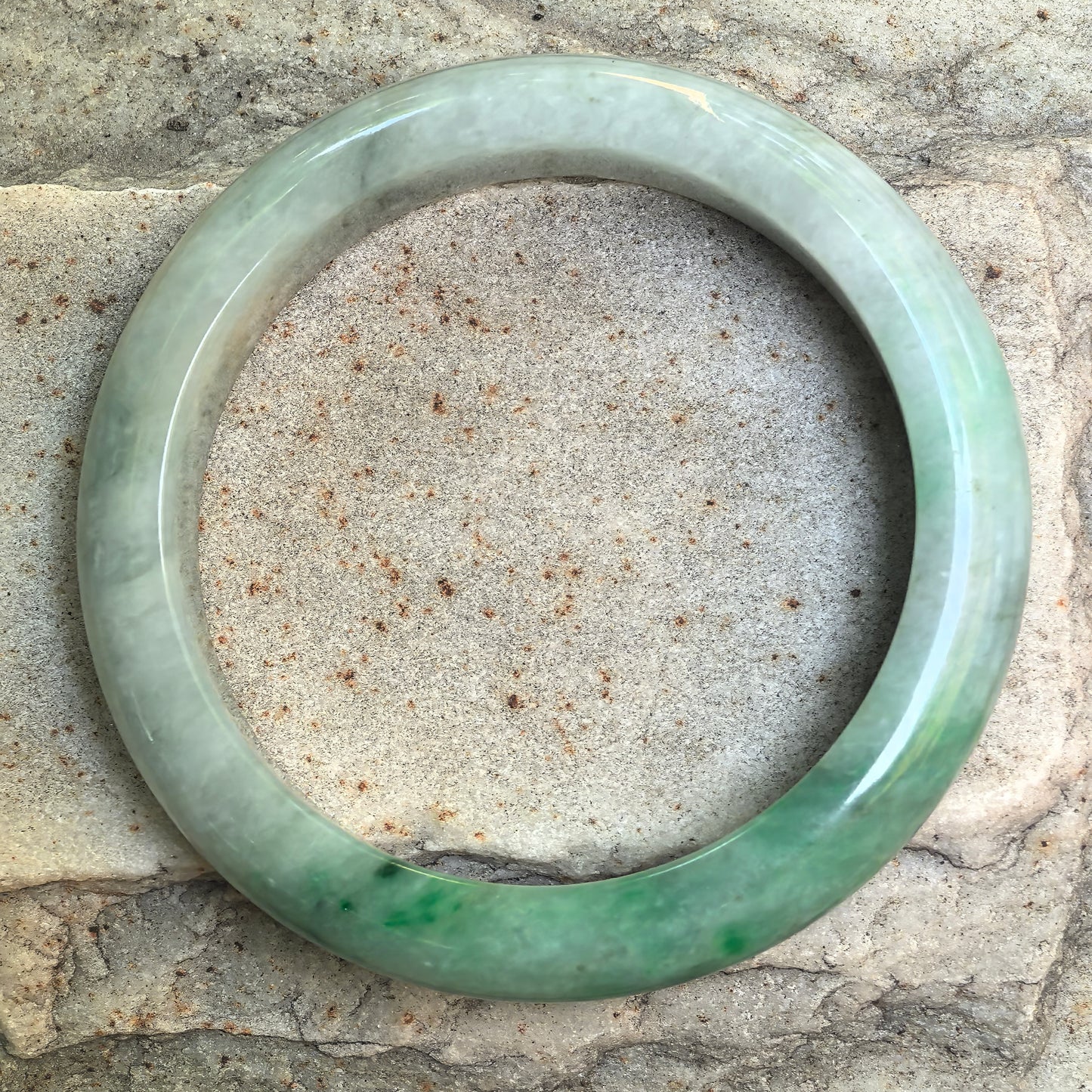 Top view of white-base green Burmese jadeite bangle showing natural dark black jadeite areas and internal texture.
