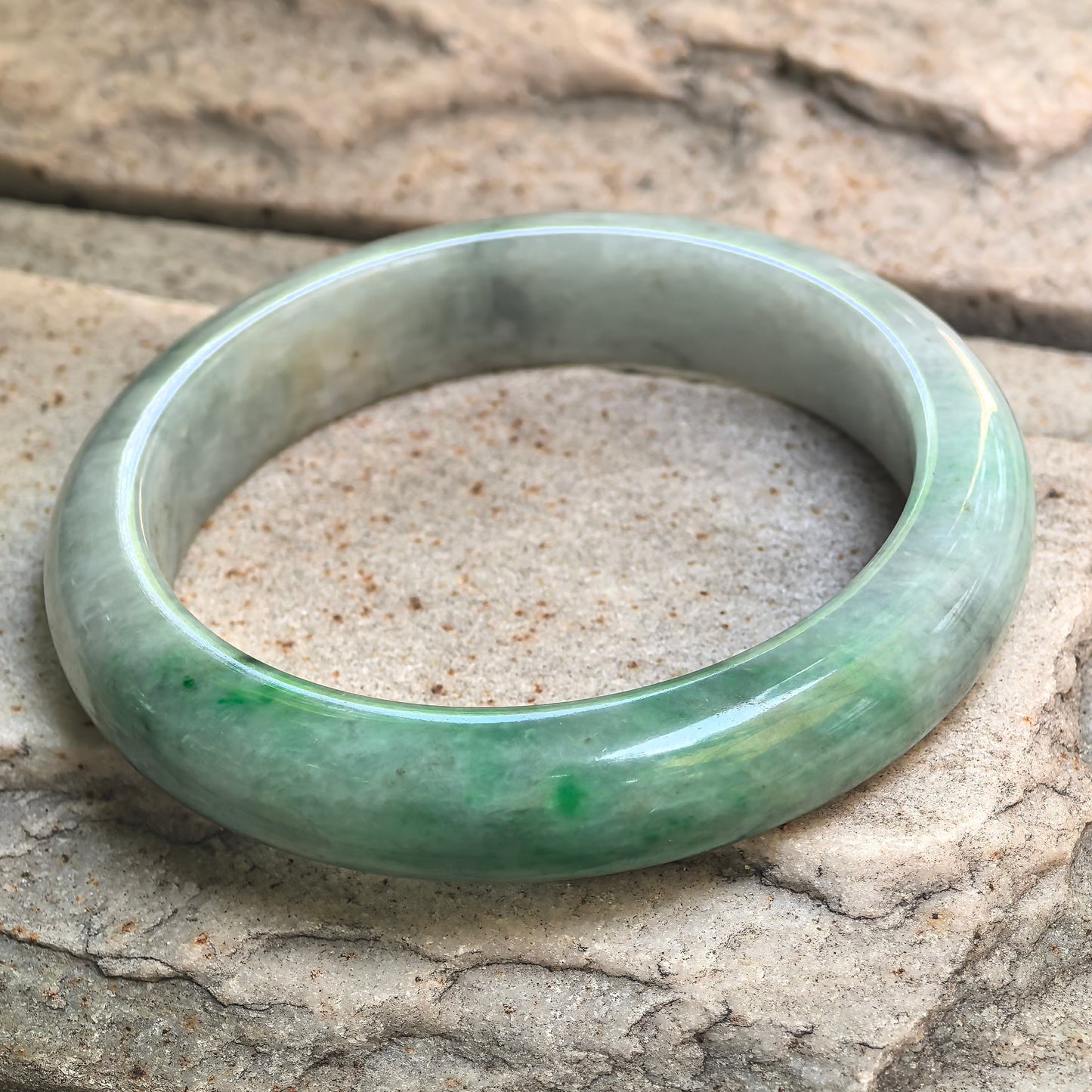 Side angle of 58mm jadeite bangle with glutinous texture, polished surface, and visible natural internal lines.