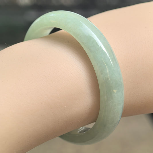 Natural Grade-A mint green oval jadeite bangle displayed on wrist with a soft glossy surface.
