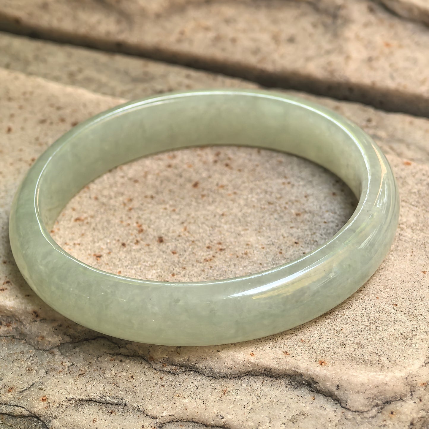 Angled view of mint green jadeite bangle on stone background showing smooth oval form.
