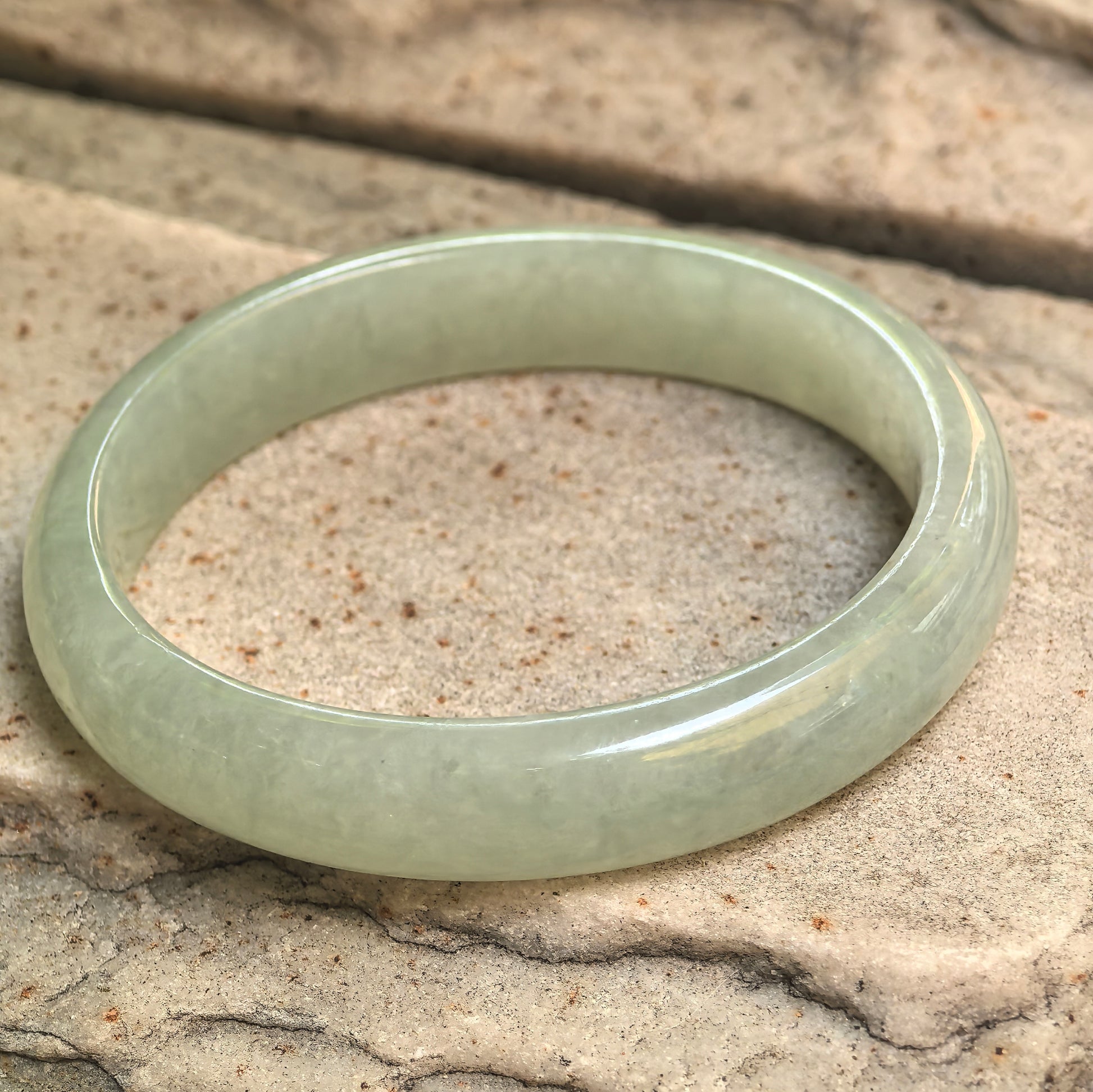 Angled view of mint green jadeite bangle on stone background showing smooth oval form.
