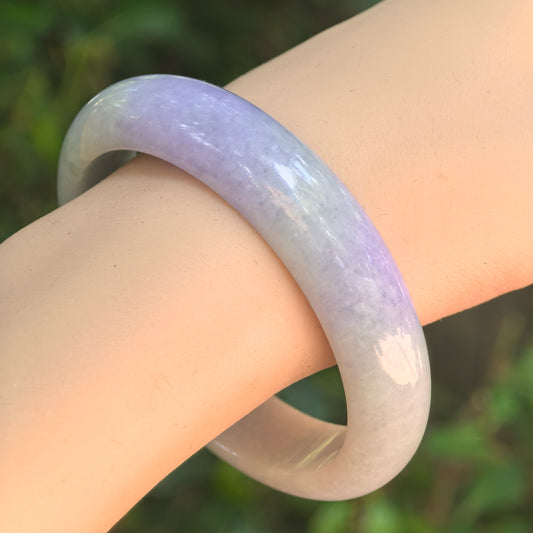 NGTC certified light green and lavender jadeite bangle worn on wrist, showing soft pastel color transition and polished surface.
