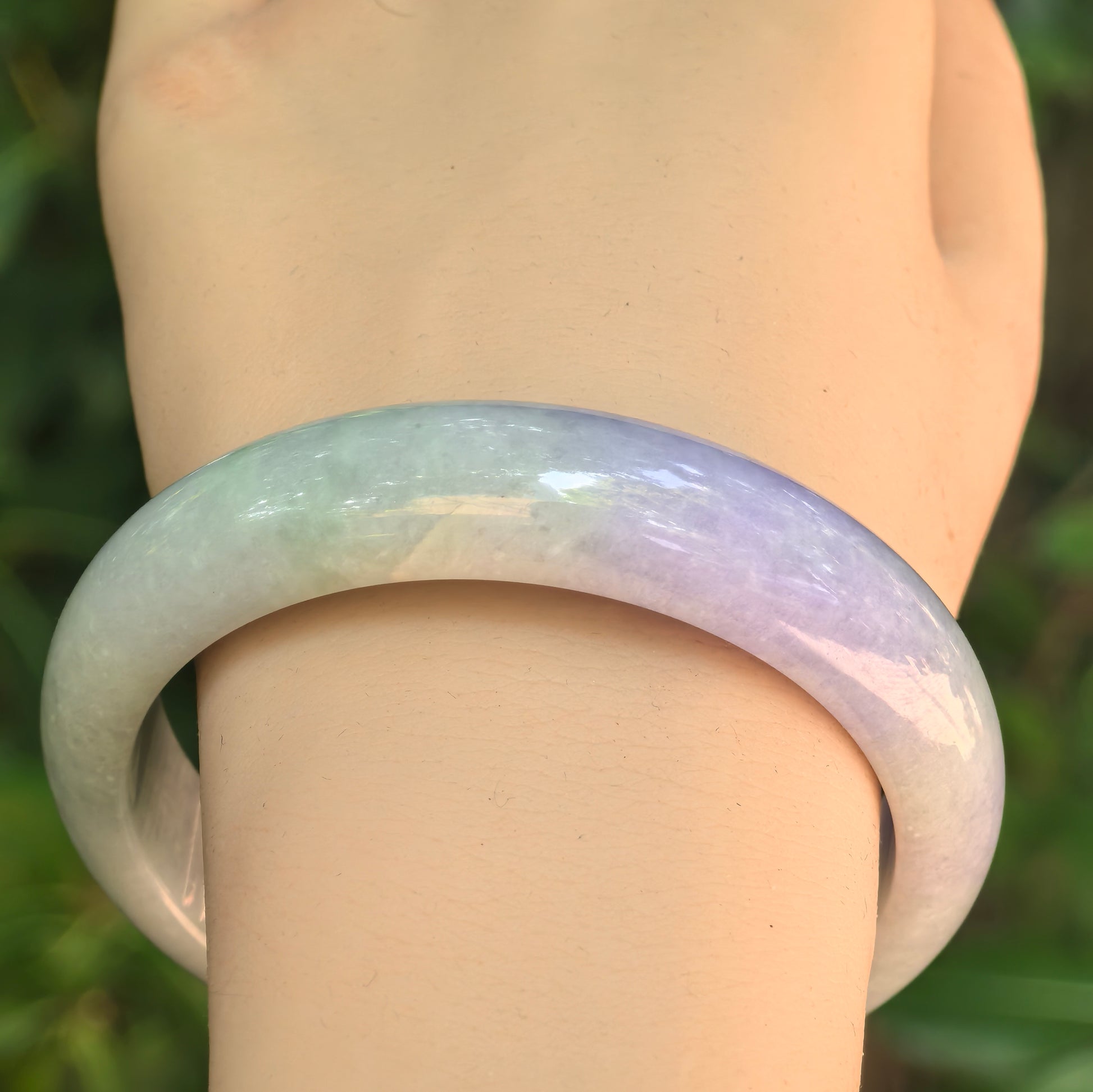 Close-up of NGTC certified bean glutinous jadeite bangle on wrist, showing lavender-purple tone and smooth rounded profile.
