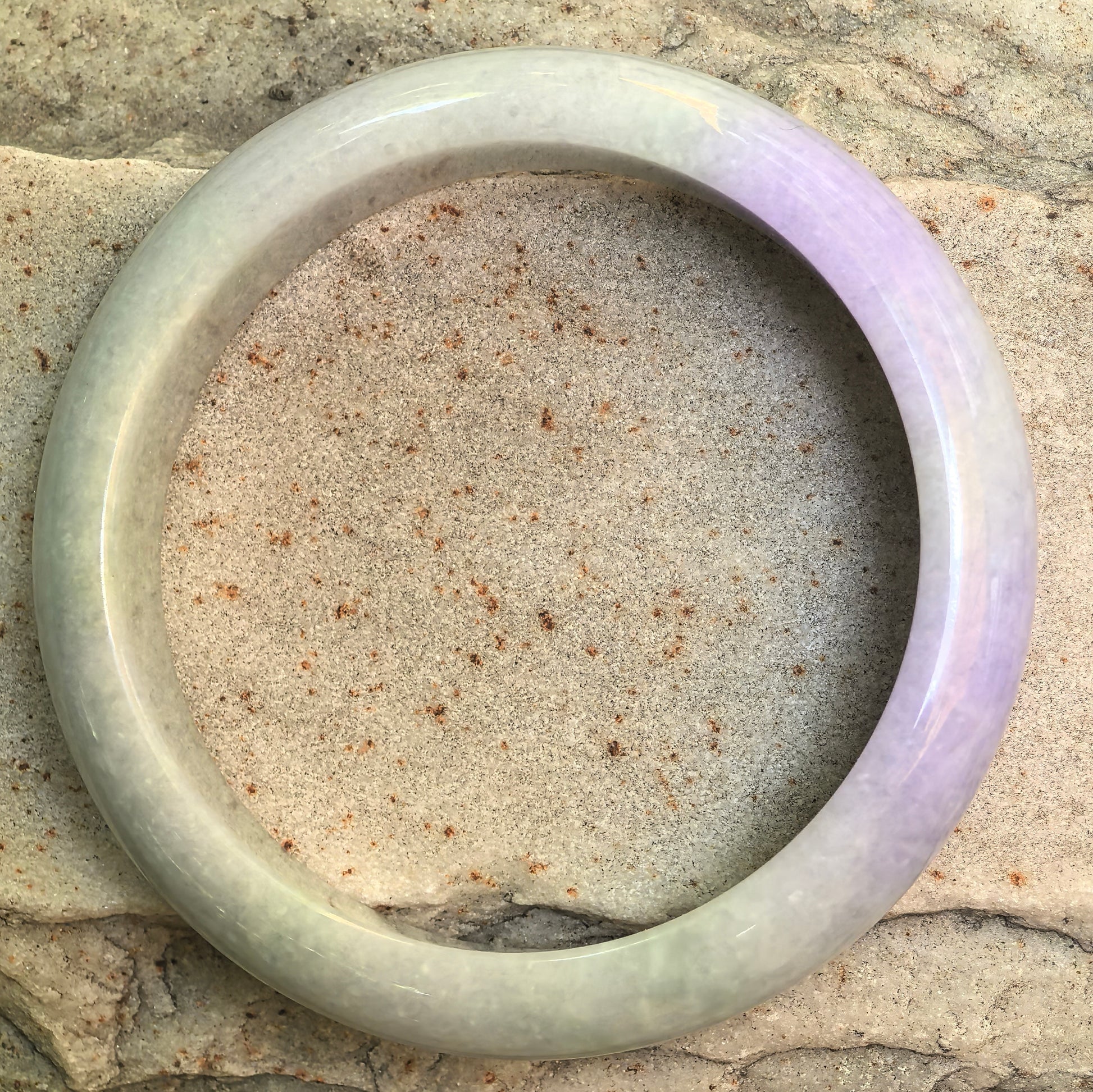 Top view of NGTC certified light green lavender D-shape jadeite bangle on stone background, showing natural two-tone color.
