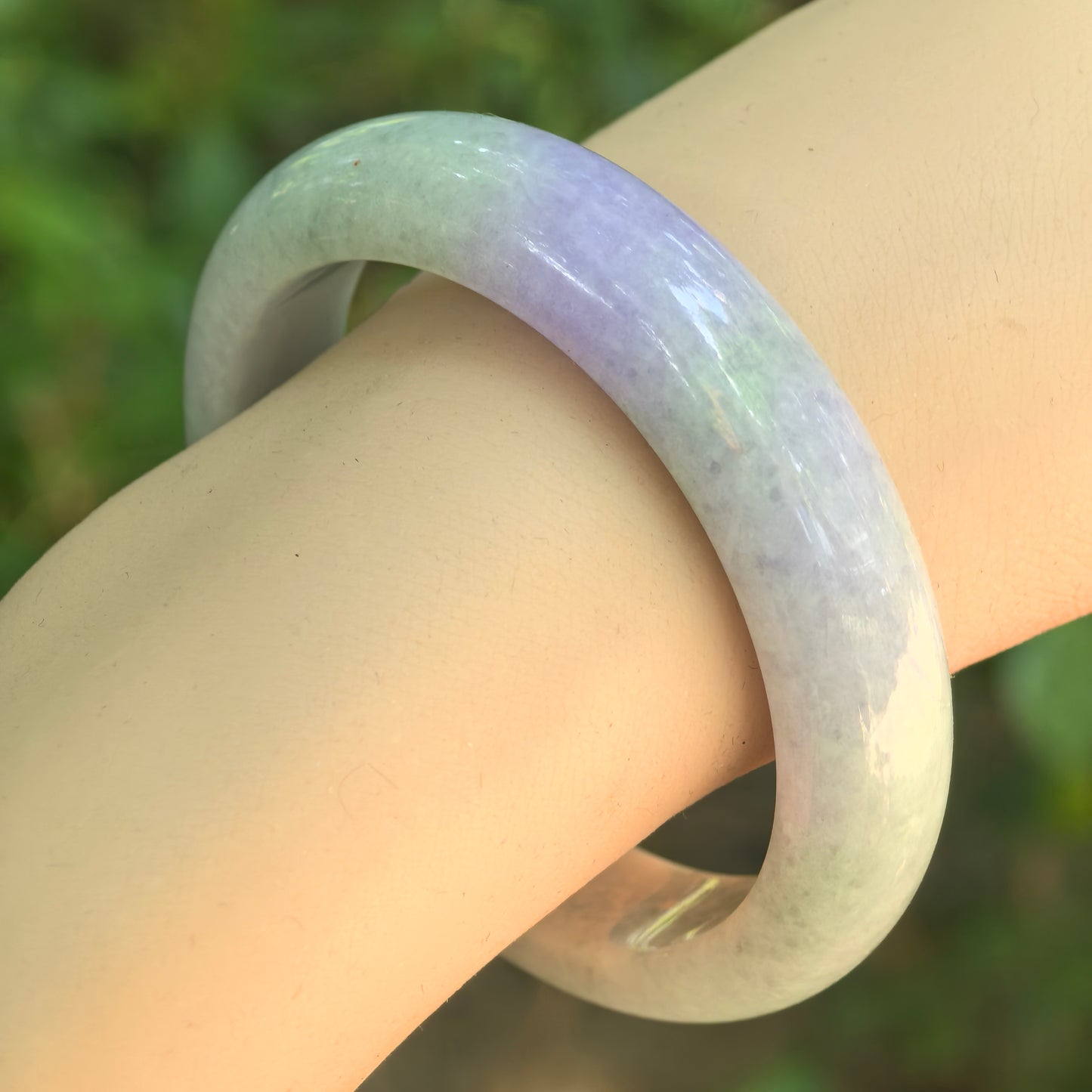 Natural Grade-A light green and lavender jadeite bangle worn on wrist, showing soft two-tone color and glossy polish.