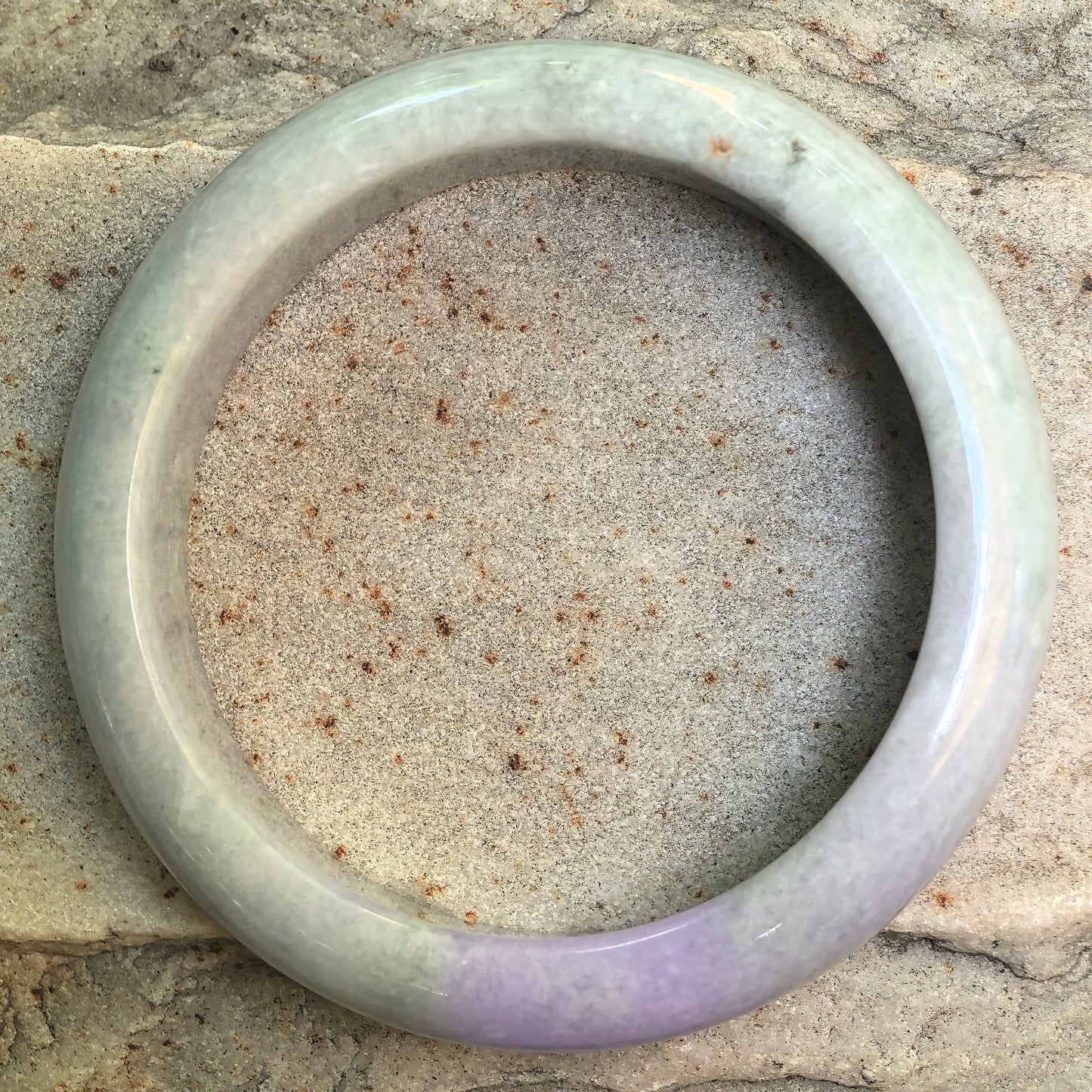 Top view of NGTC certified jadeite bangle on stone background, showing round ring form and soft green lavender color transition.
