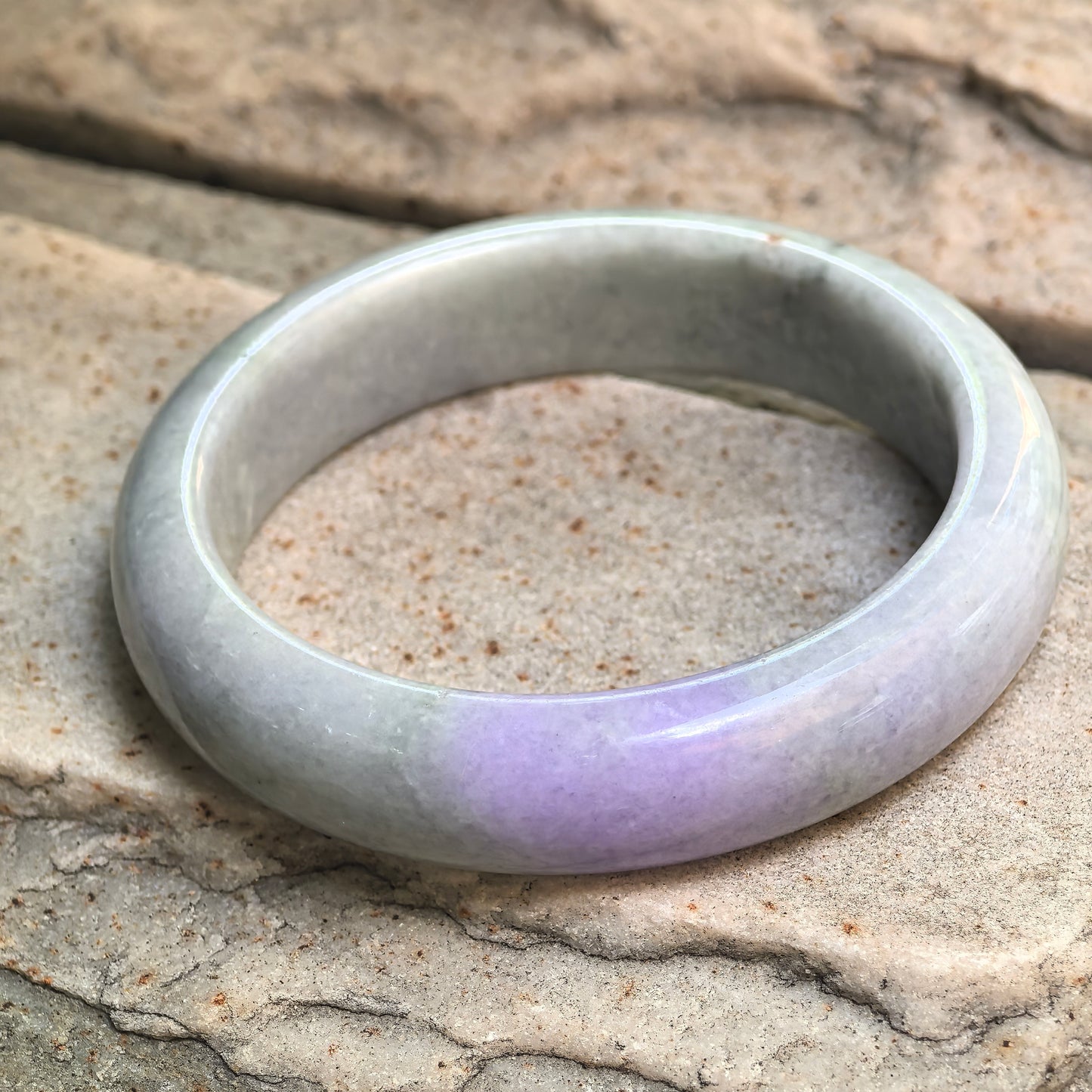 Angled side view of light green lavender D-shape jadeite bangle, showing medium-wide body, smooth polish, and natural surface details.