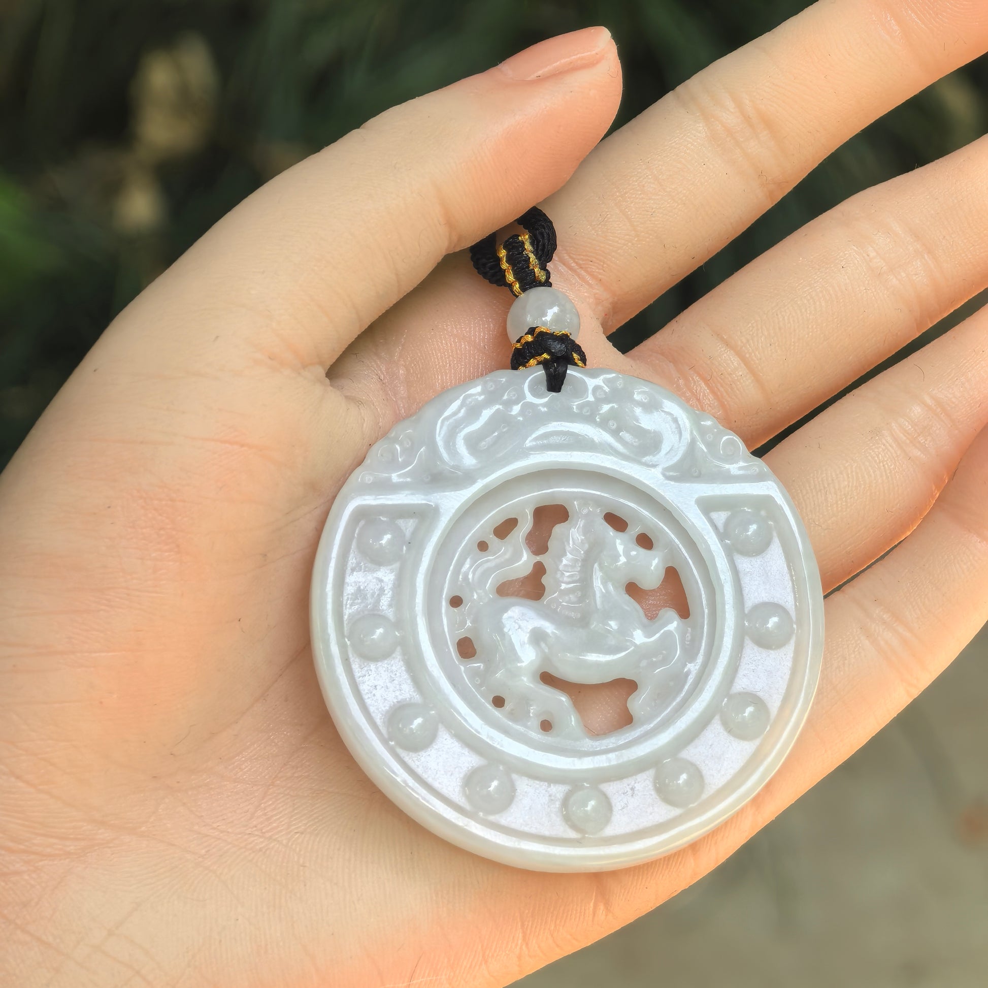 White jadeite horse plaque pendant shown in hand, featuring a rotatable inner horse motif and raised outer bead details.