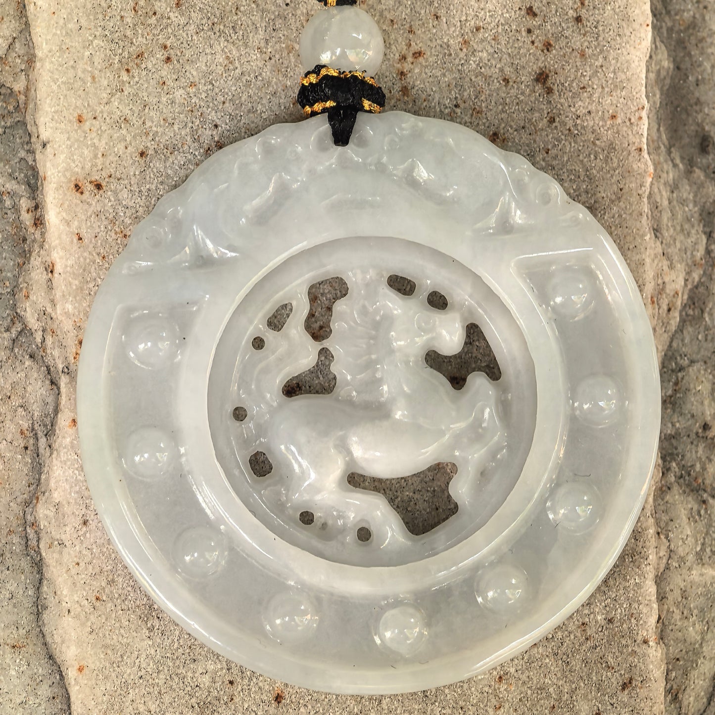 Close-up of glutinous white jadeite pendant showing openwork horse carving, smooth polish, and soft translucency.