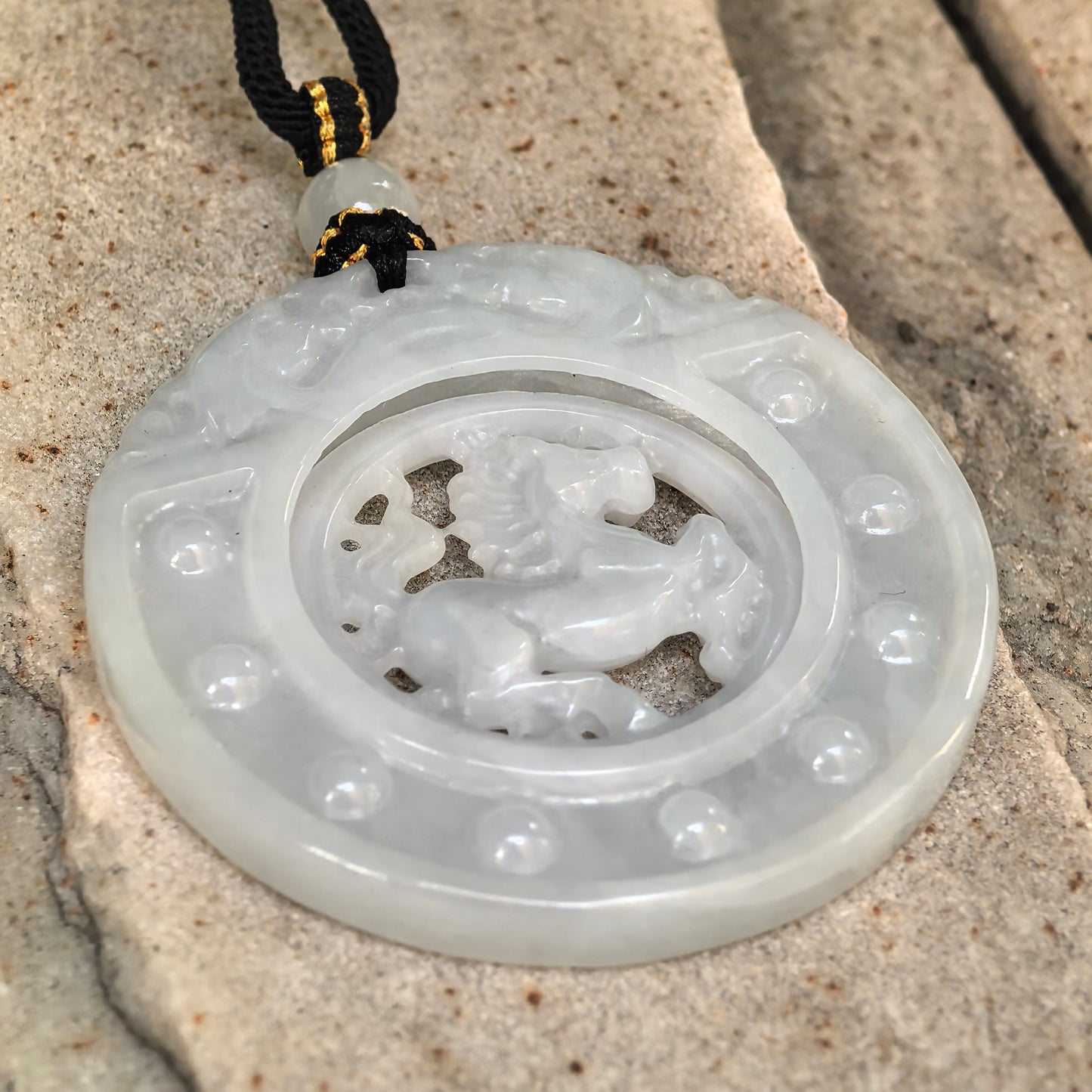 Side view of round white jadeite horse plaque pendant on stone surface showing layered carving and pendant thickness.