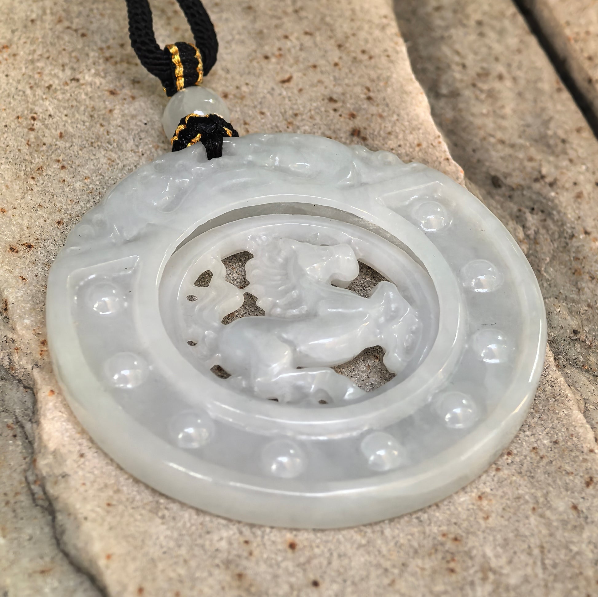 Side view of round white jadeite horse plaque pendant on stone surface showing layered carving and pendant thickness.