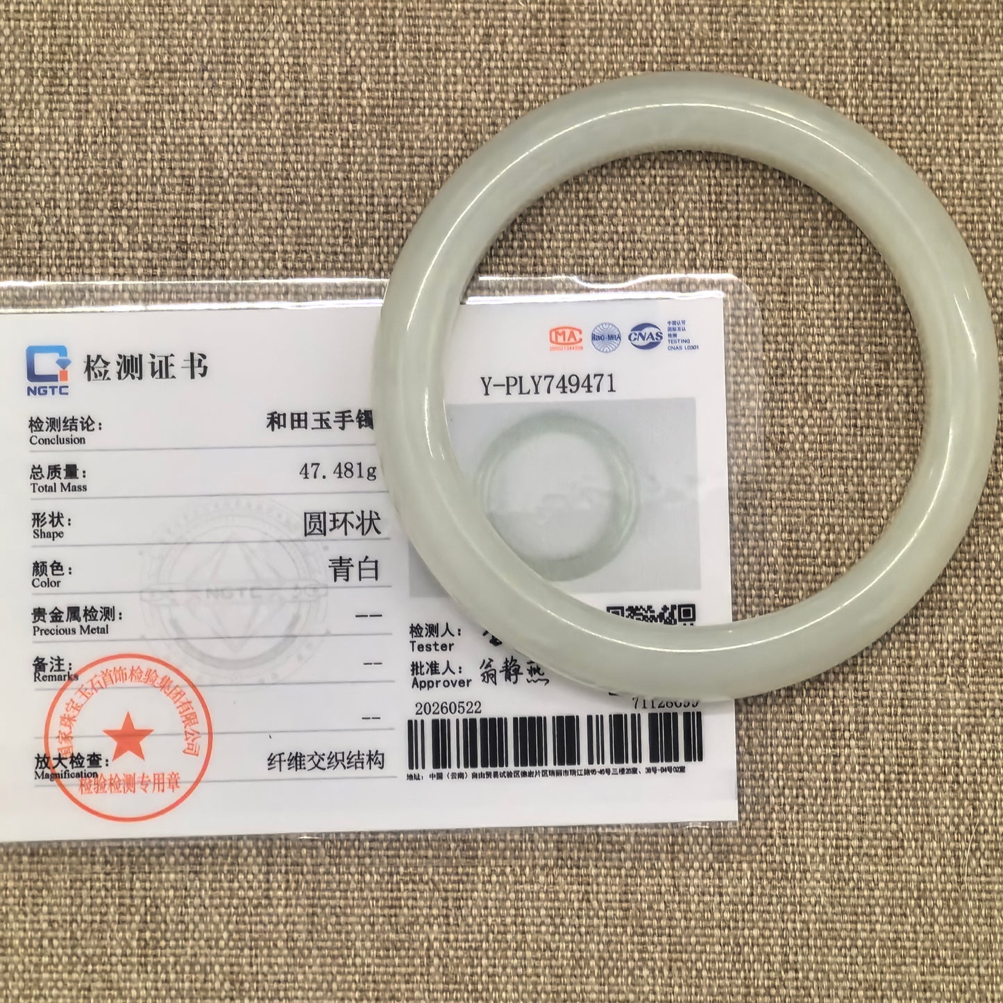 NGTC certified Hetian jade bangle displayed with certificate, showing pale green-white color and round bangle shape.