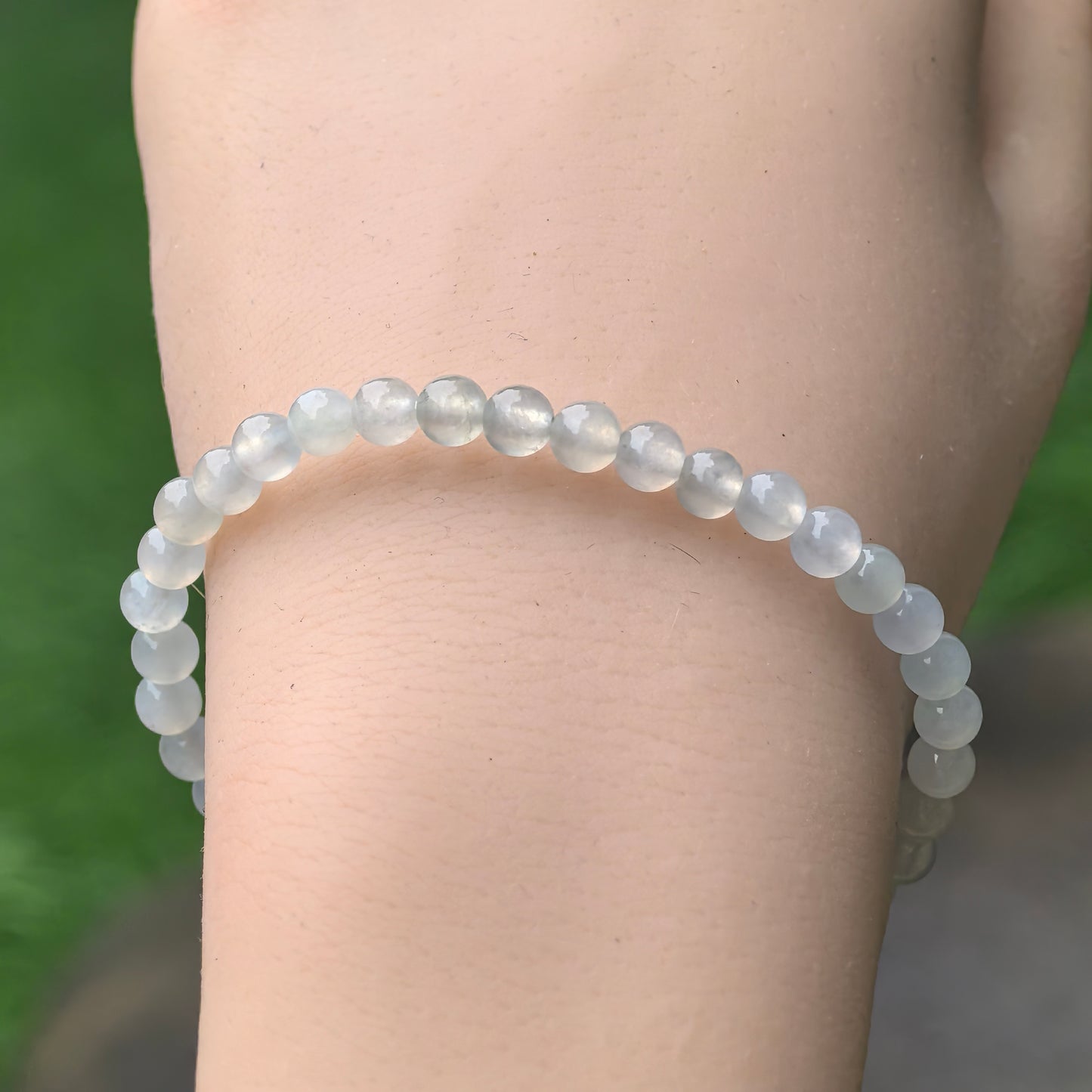 Side view of small round jadeite bead bracelet worn on wrist with subtle green undertone.
