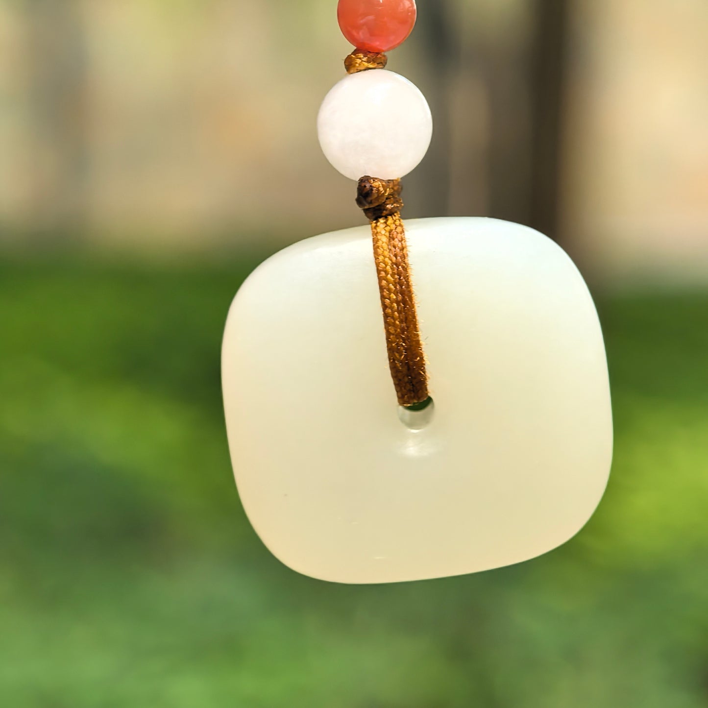Natural white Hetian jade square Peace Pendant hanging outdoors with brown cord and accent beads.