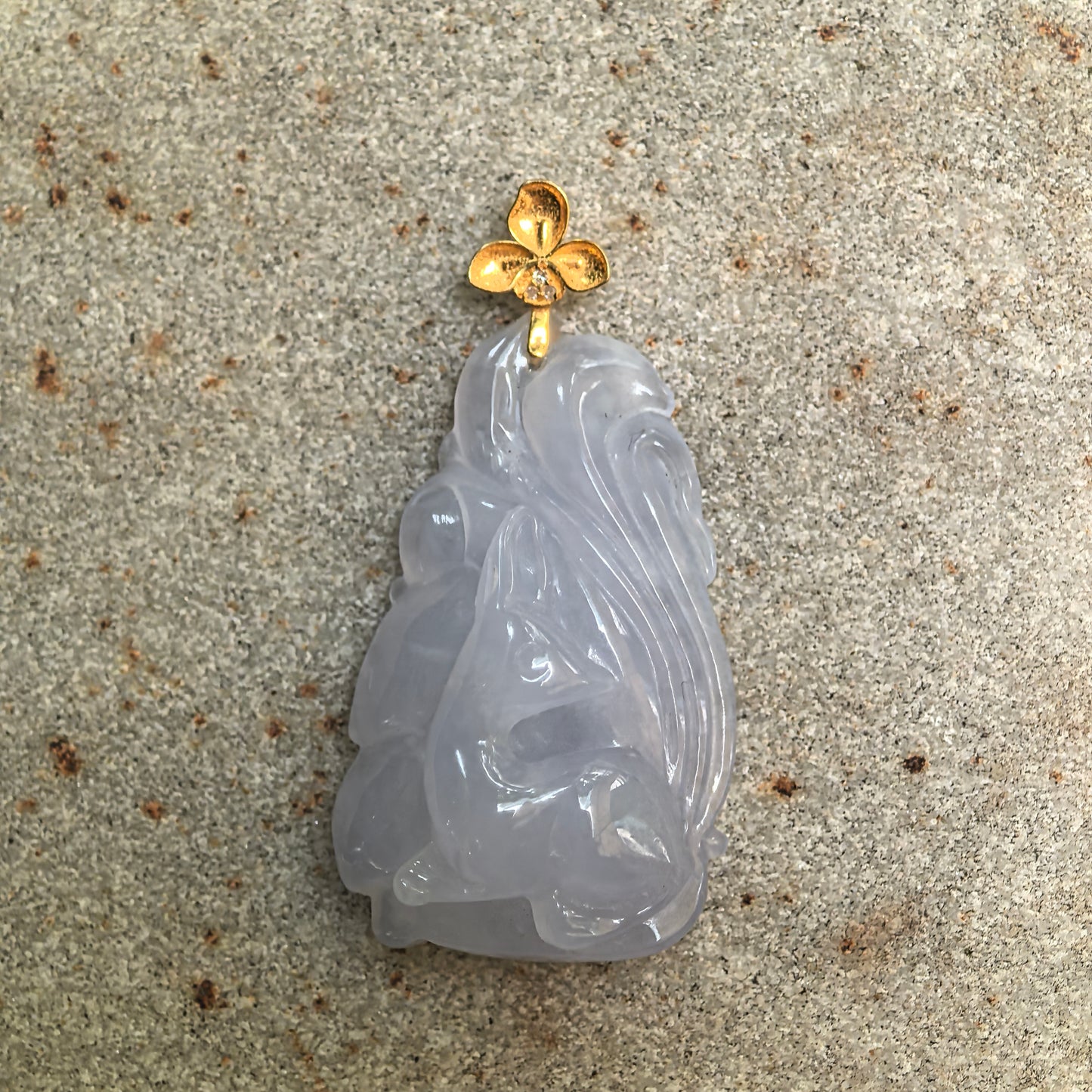 Natural Grade-A icy glutinous lavender nine-tailed fox jadeite pendant with 18K gold flower bail on stone background.
