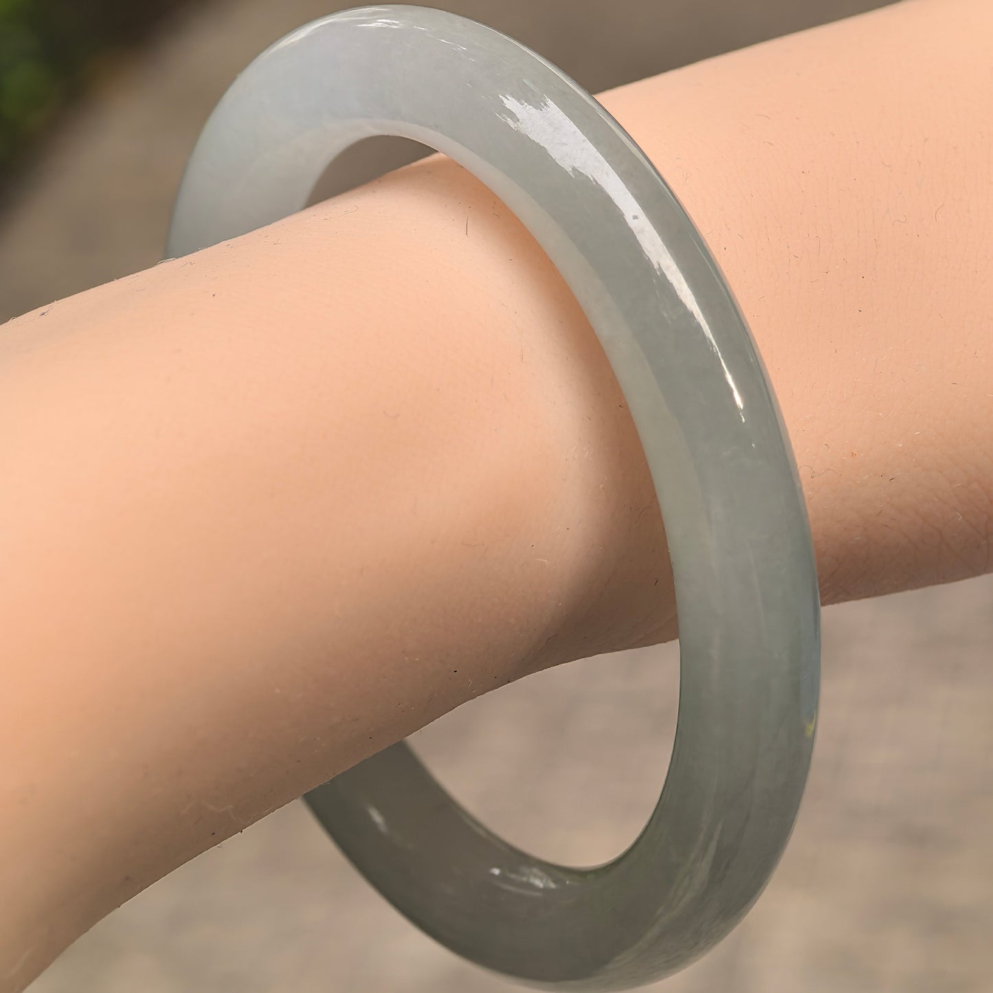 Natural Grade-A icy glutinous pale green round jadeite bangle shown on wrist with soft glossy surface.