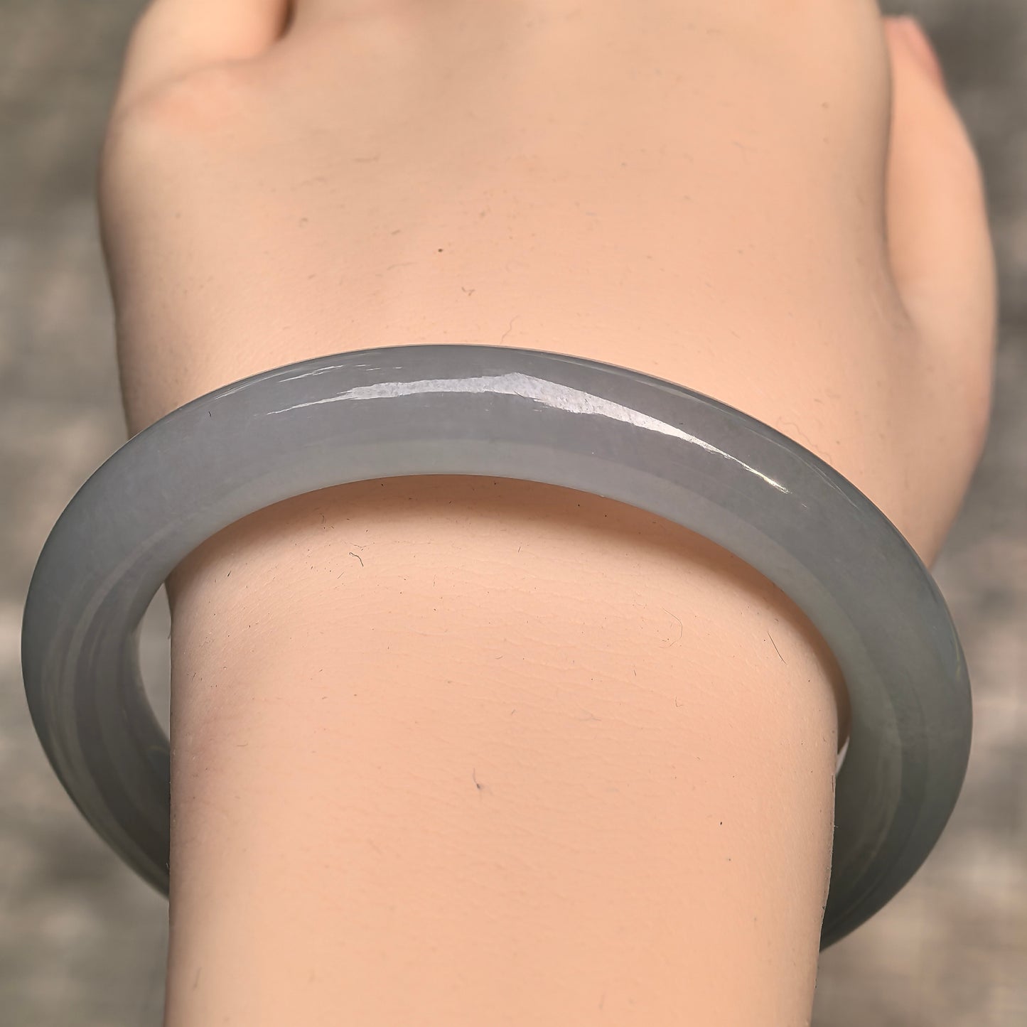 Close-up wrist view of icy glutinous pale green jadeite bangle showing soft translucency and rounded shape.