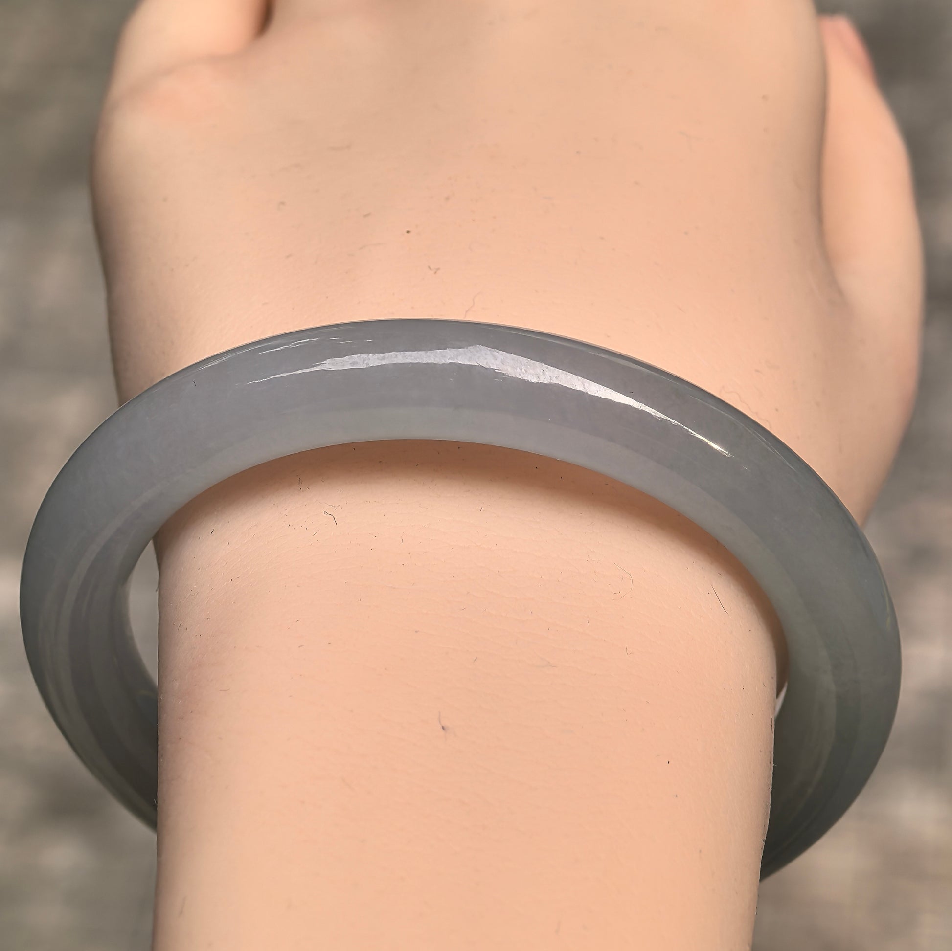Close-up wrist view of icy glutinous pale green jadeite bangle showing soft translucency and rounded shape.