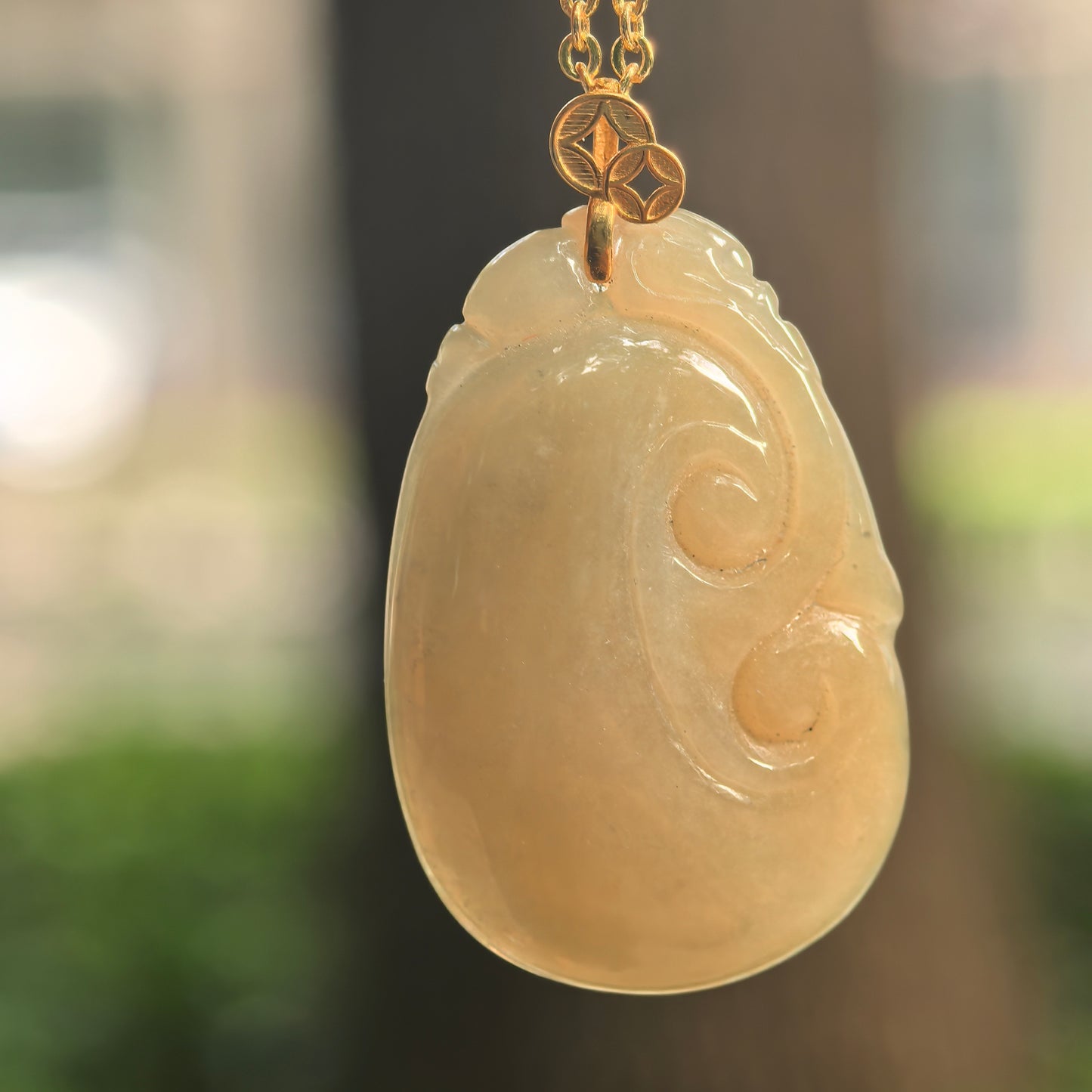 Natural Grade-A glutinous yellow Ruyi jadeite pendant with gold bail hanging under soft light.