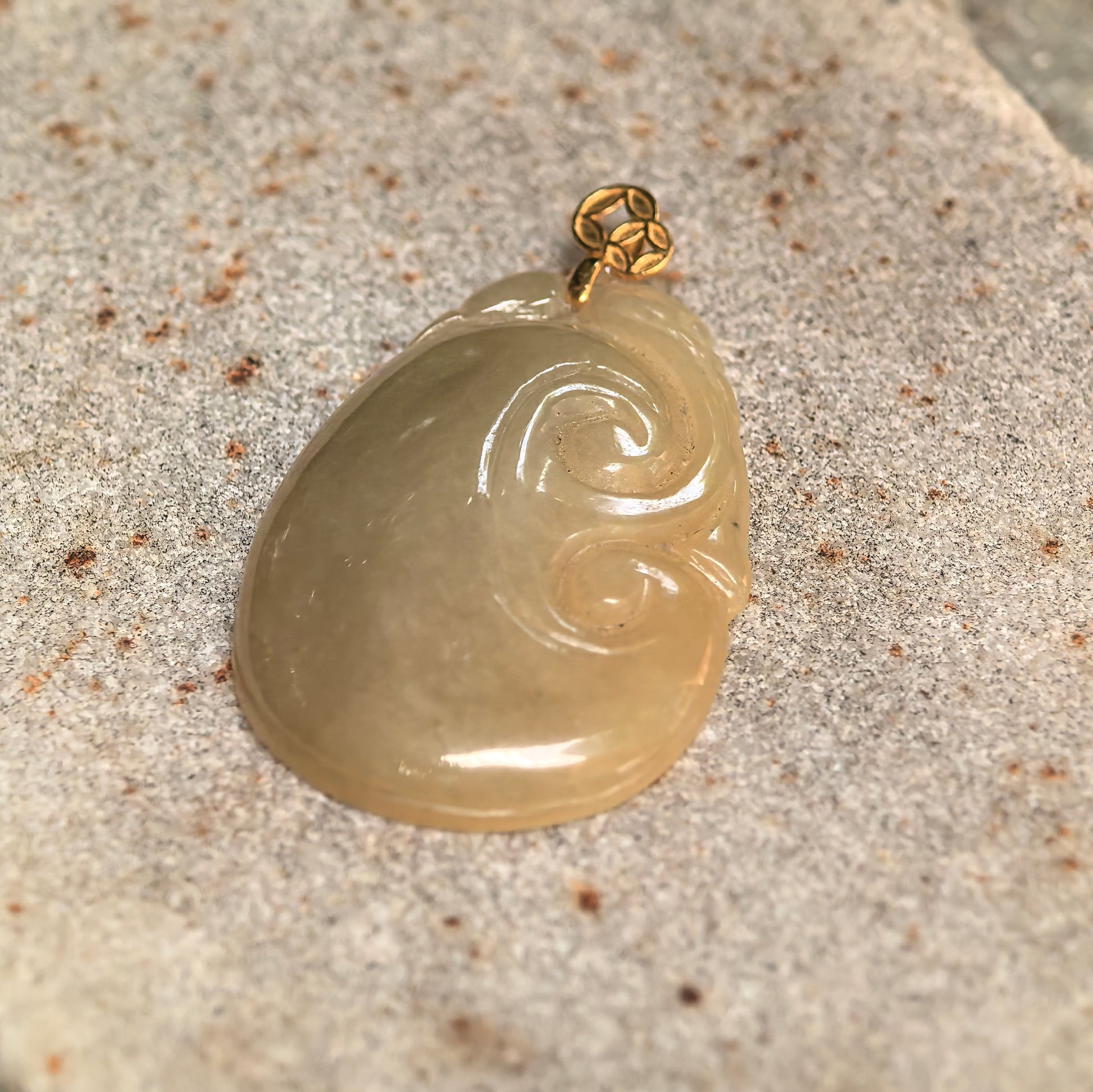 Close-up of glutinous yellow Ruyi jadeite pendant on stone background with curved carving details.