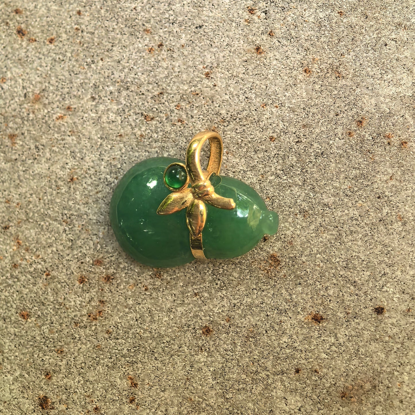 Natural Grade-A light green jadeite gourd pendant with 18K gold floral detail displayed on stone background.
