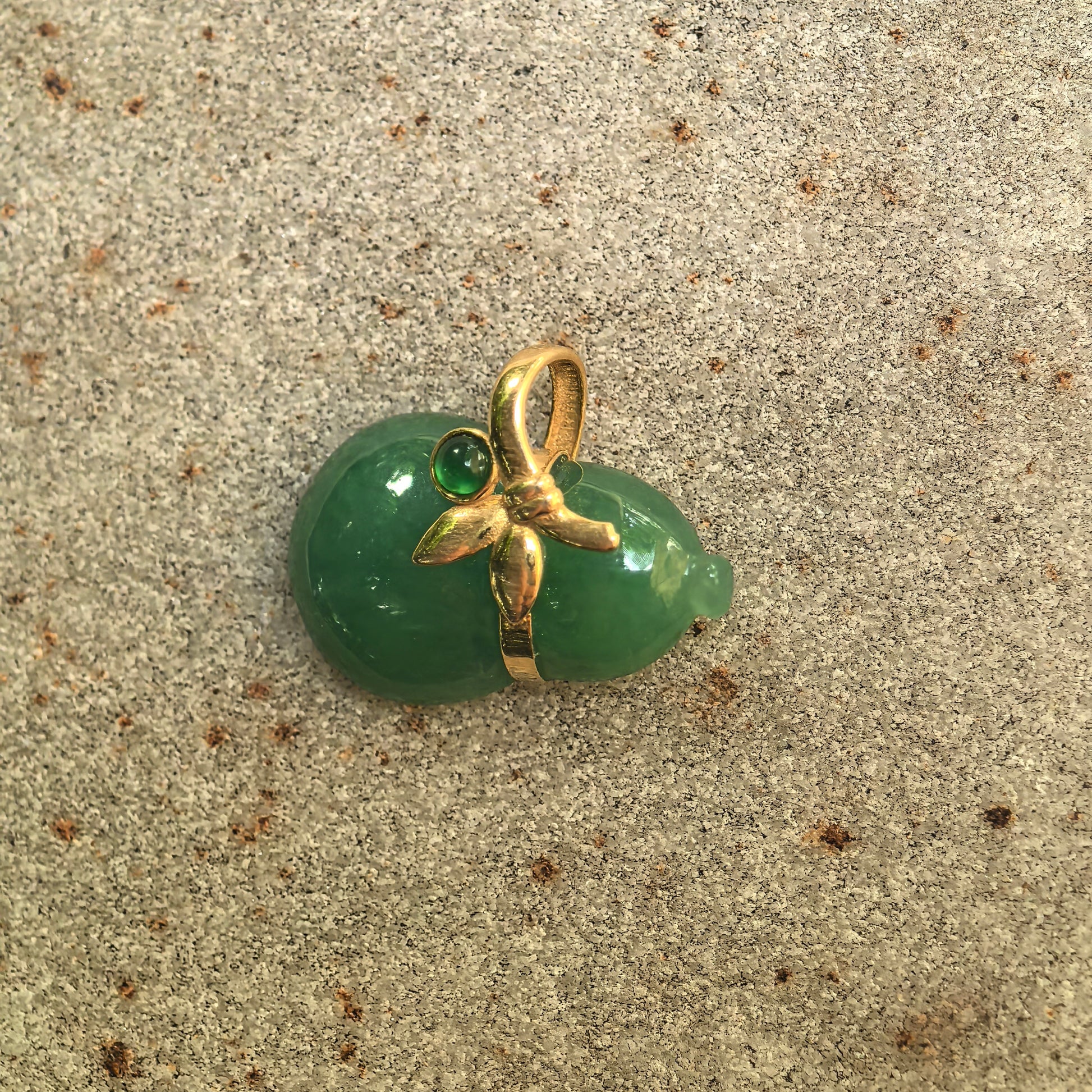 Natural Grade-A light green jadeite gourd pendant with 18K gold floral detail displayed on stone background.