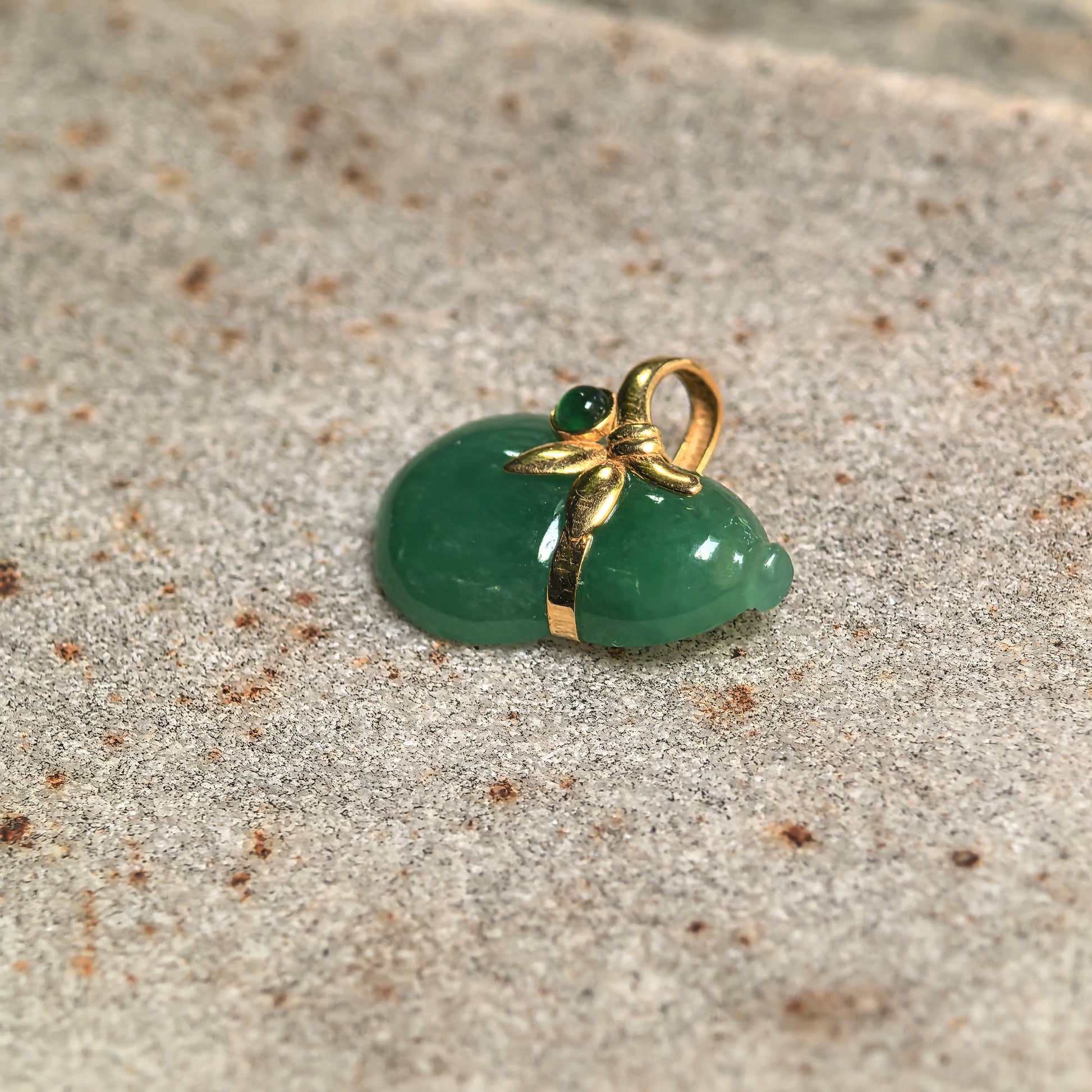 Side view of small glutinous green jadeite gourd pendant with polished surface and gold setting.