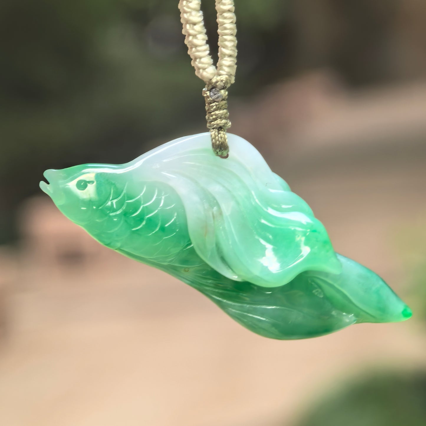 Natural Grade-A fine glutinous green jadeite fish pendant hanging with cord, showing vivid green and light green tones.