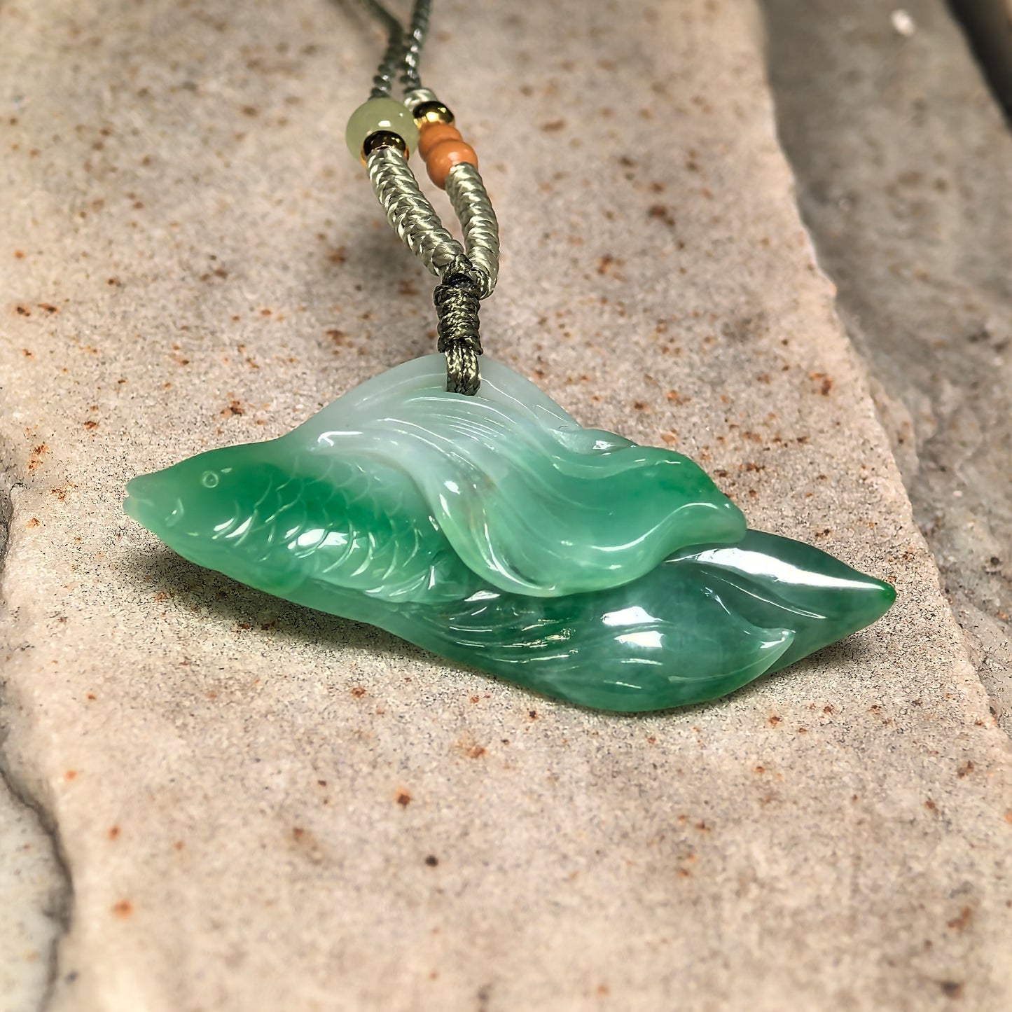 Side view of carved jadeite fish pendant showing elongated shape, glossy polish, and raised carved details.