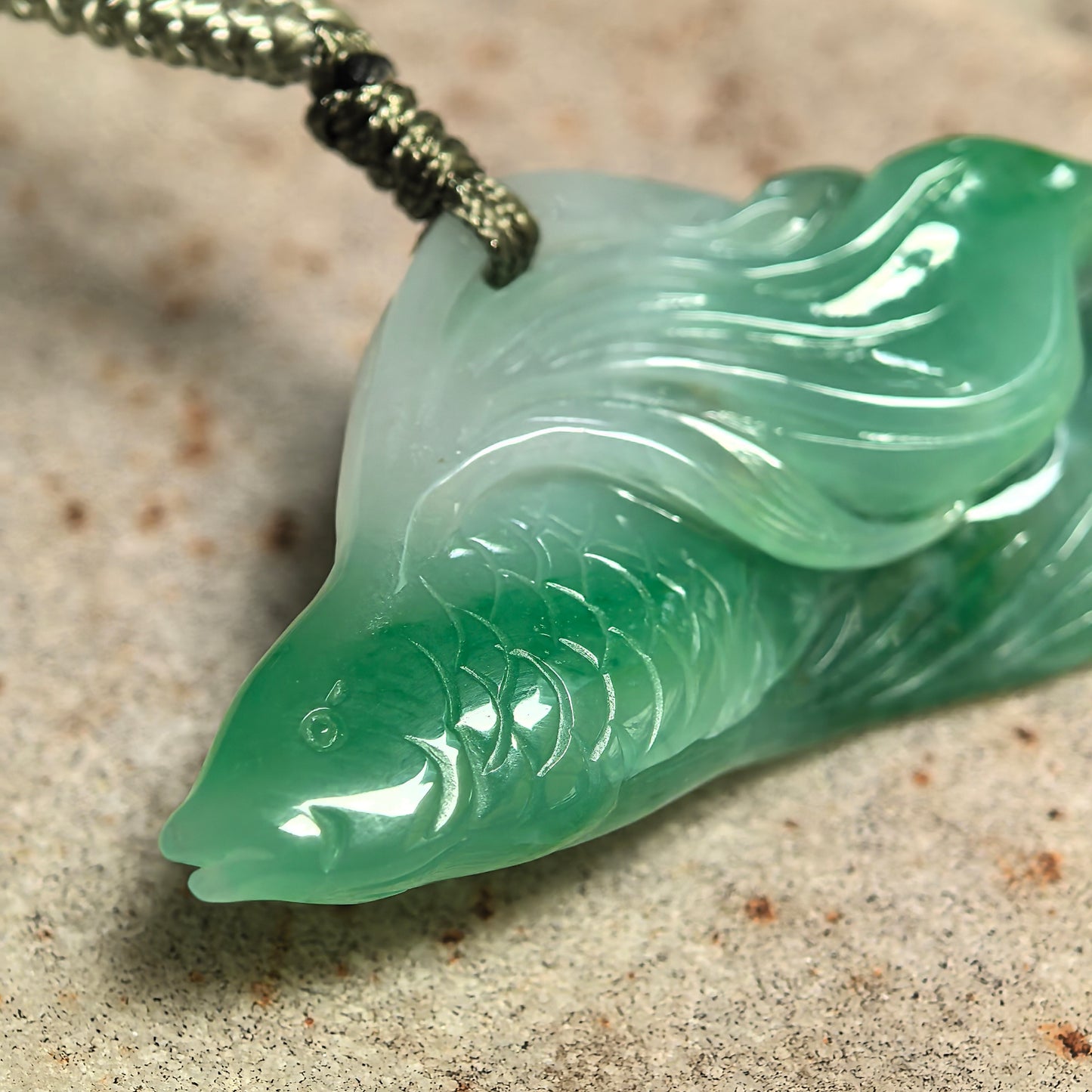 Close-up of natural jadeite fish carving showing fish scales, raised eye, and layered green translucency.