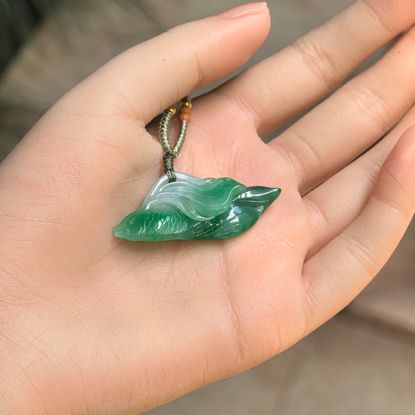 Natural Grade-A green jadeite fish pendant shown in hand, displaying compact wearable size and vivid fish carving.